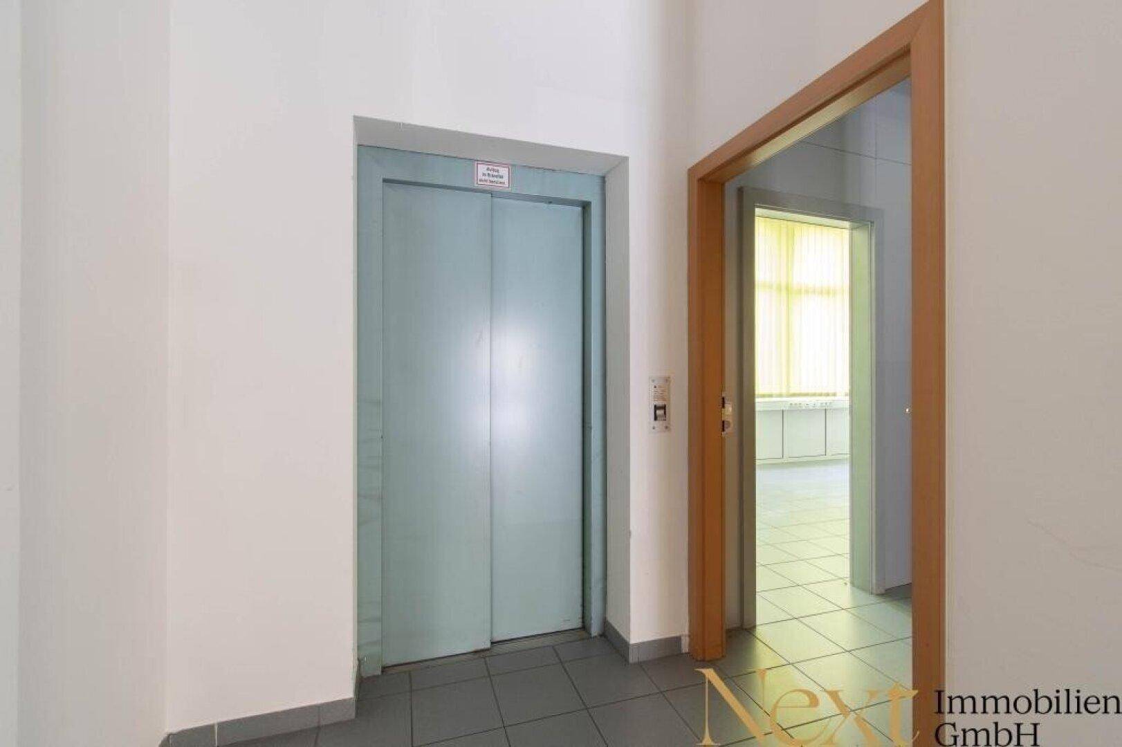 Flur mit einem Aufzug und Zugang zu weiteren Räumlichkeiten, ausgestattet mit Fliesenboden.