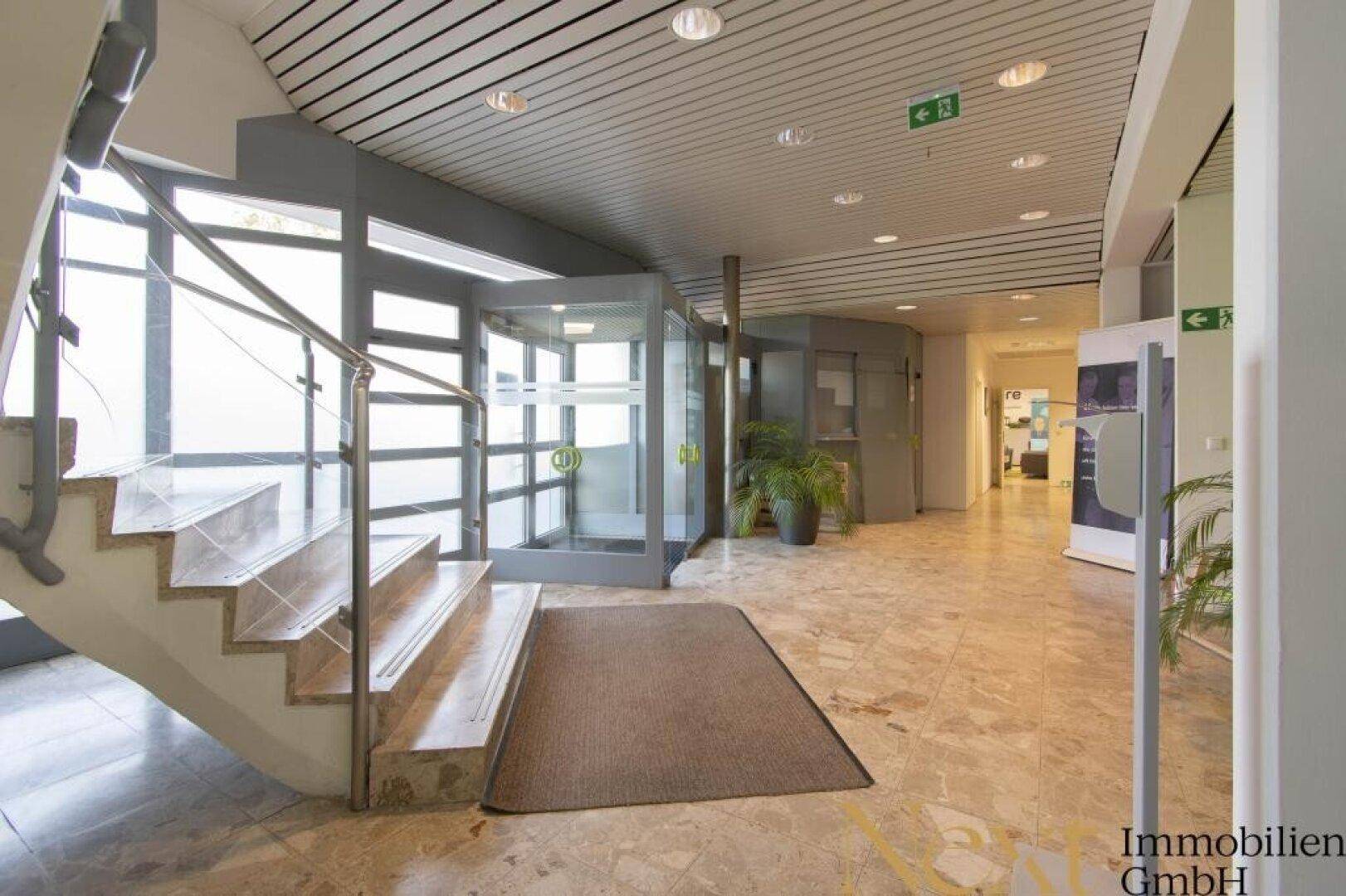 Heller Eingangsbereich mit Marmorboden, Treppe und moderner Drehtür, einladend gestaltet.