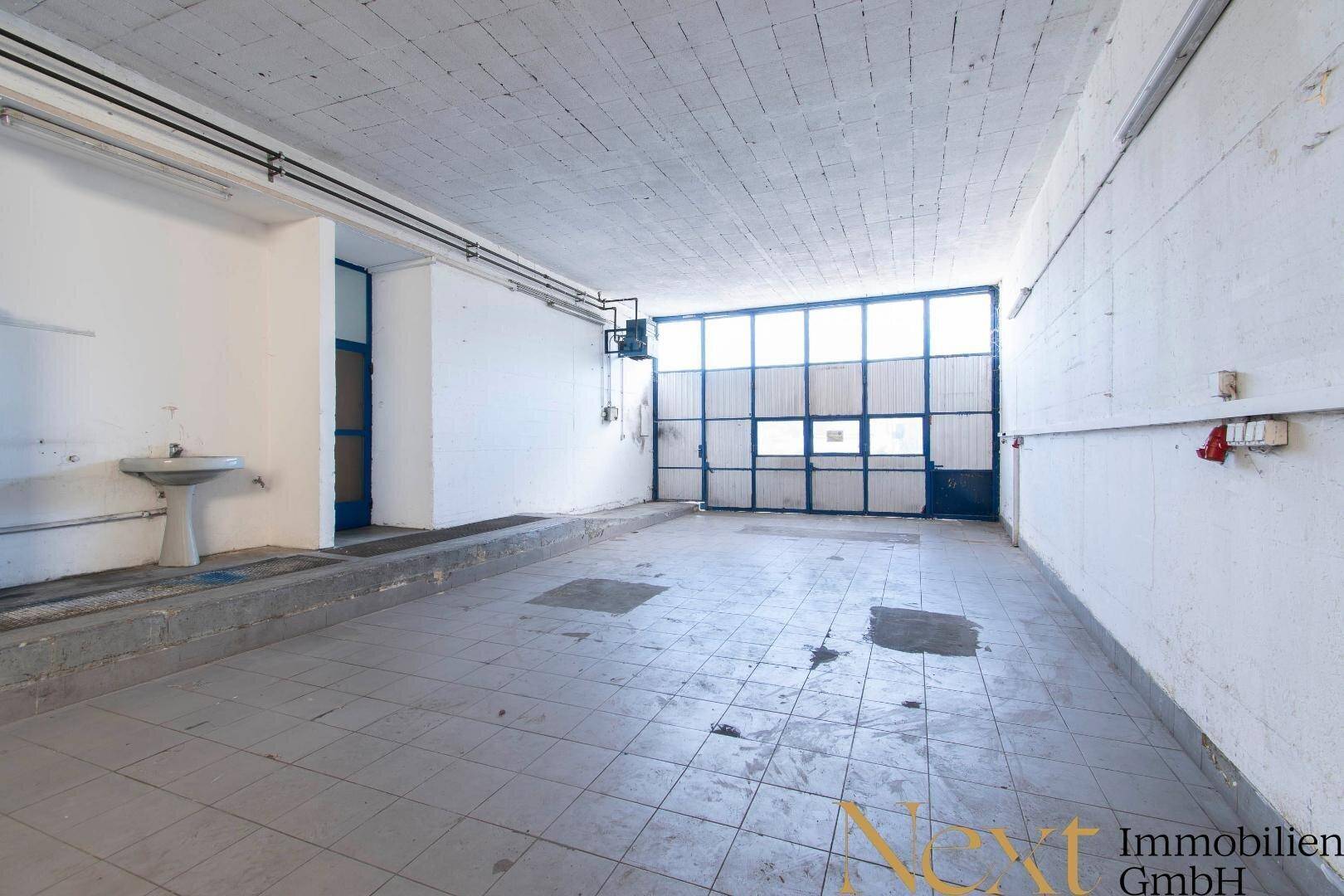 Geräumige Garage mit großem Rolltor, gefliestem Boden und Waschbecken, ideal für Fahrzeuge oder Lagerung.