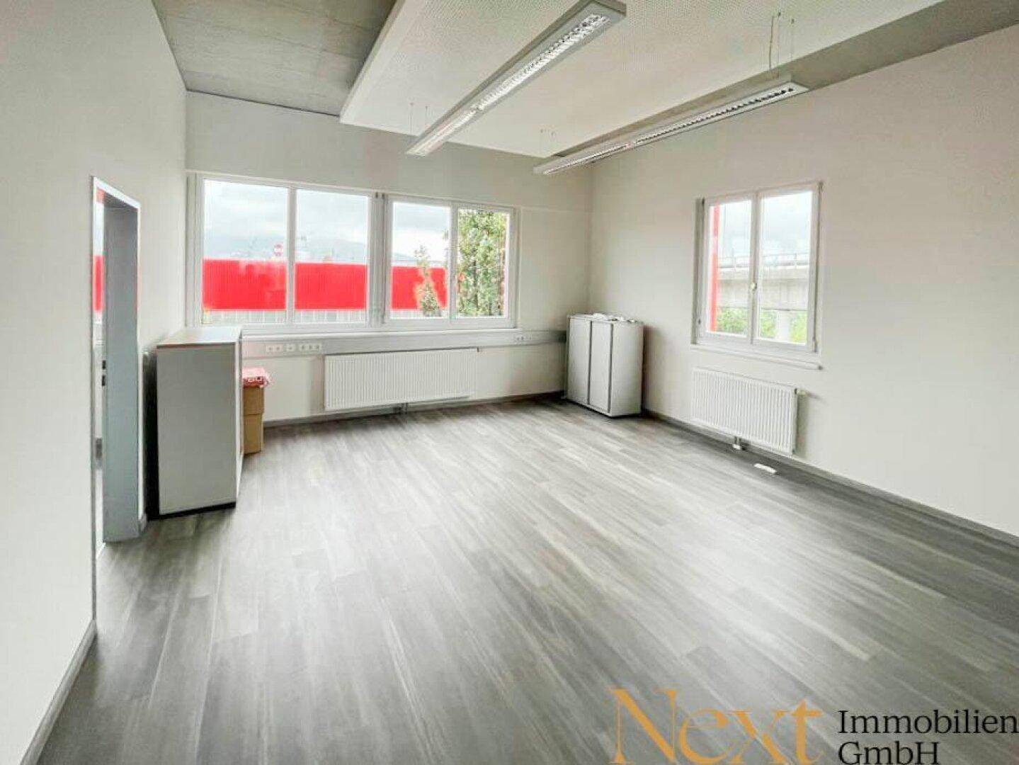 Helles Büro mit großen Fenstern, modernem Laminatboden und Heizkörpern, bietet viel Tageslicht für Arbeitsplätze.