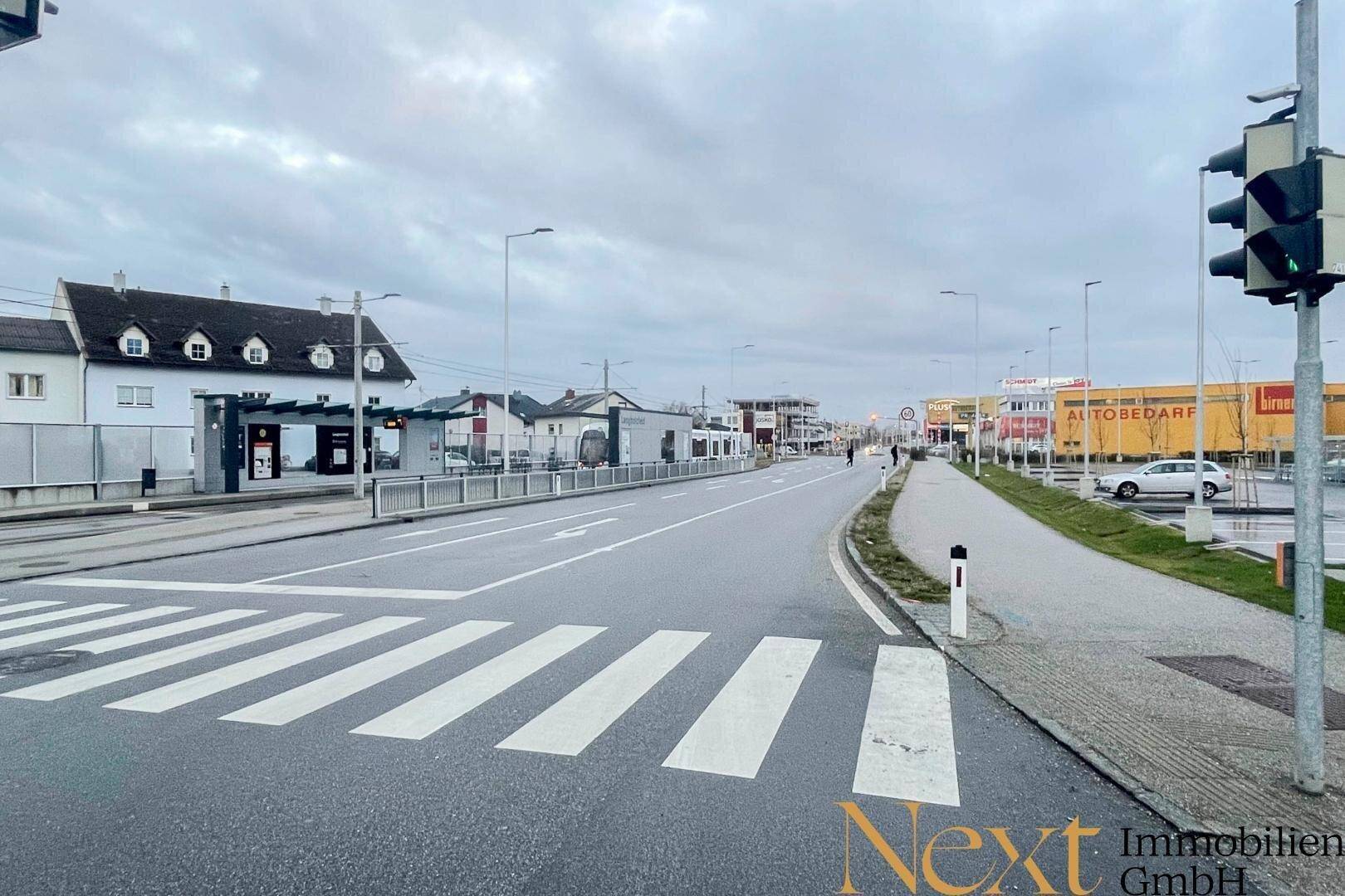 Blick auf eine belebte Straße mit Zebrastreifen, Ampel und Gewerbegebäuden im Hintergrund an einem bewölkten Tag.
