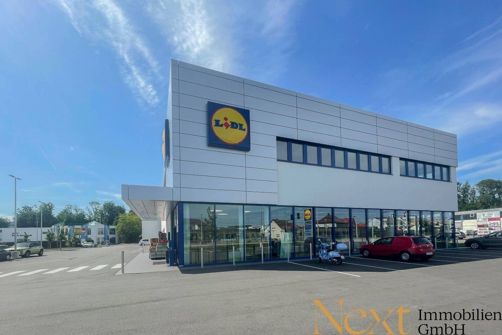 Seitenansicht des modernen Supermarktgebäudes mit großen Fenstern, Eingangsbereich und Parkplätzen.