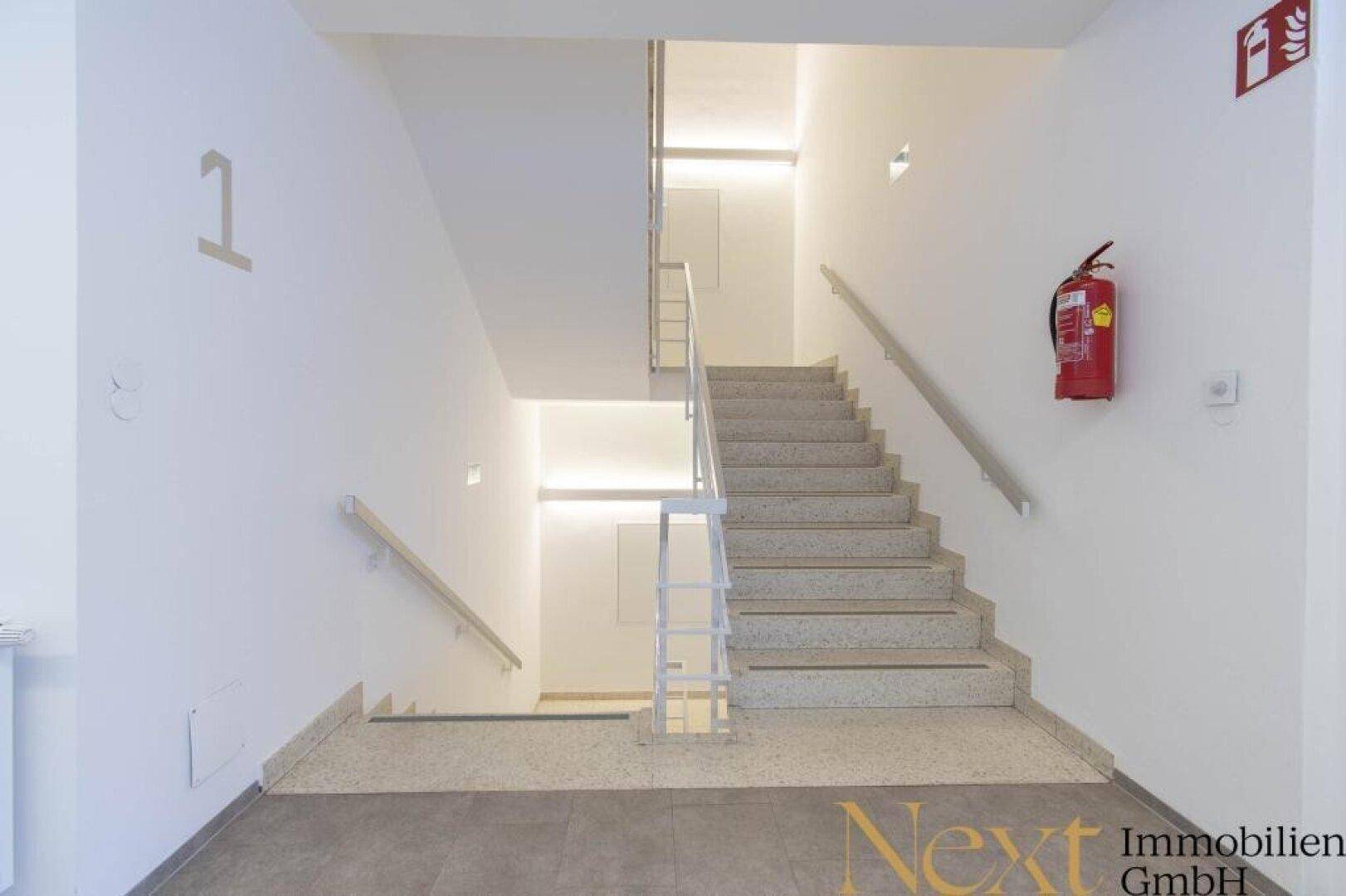 Helles Treppenhaus mit Terrazzostufen und Metallgeländer, das die verschiedenen Etagen des Gebäudes verbindet.