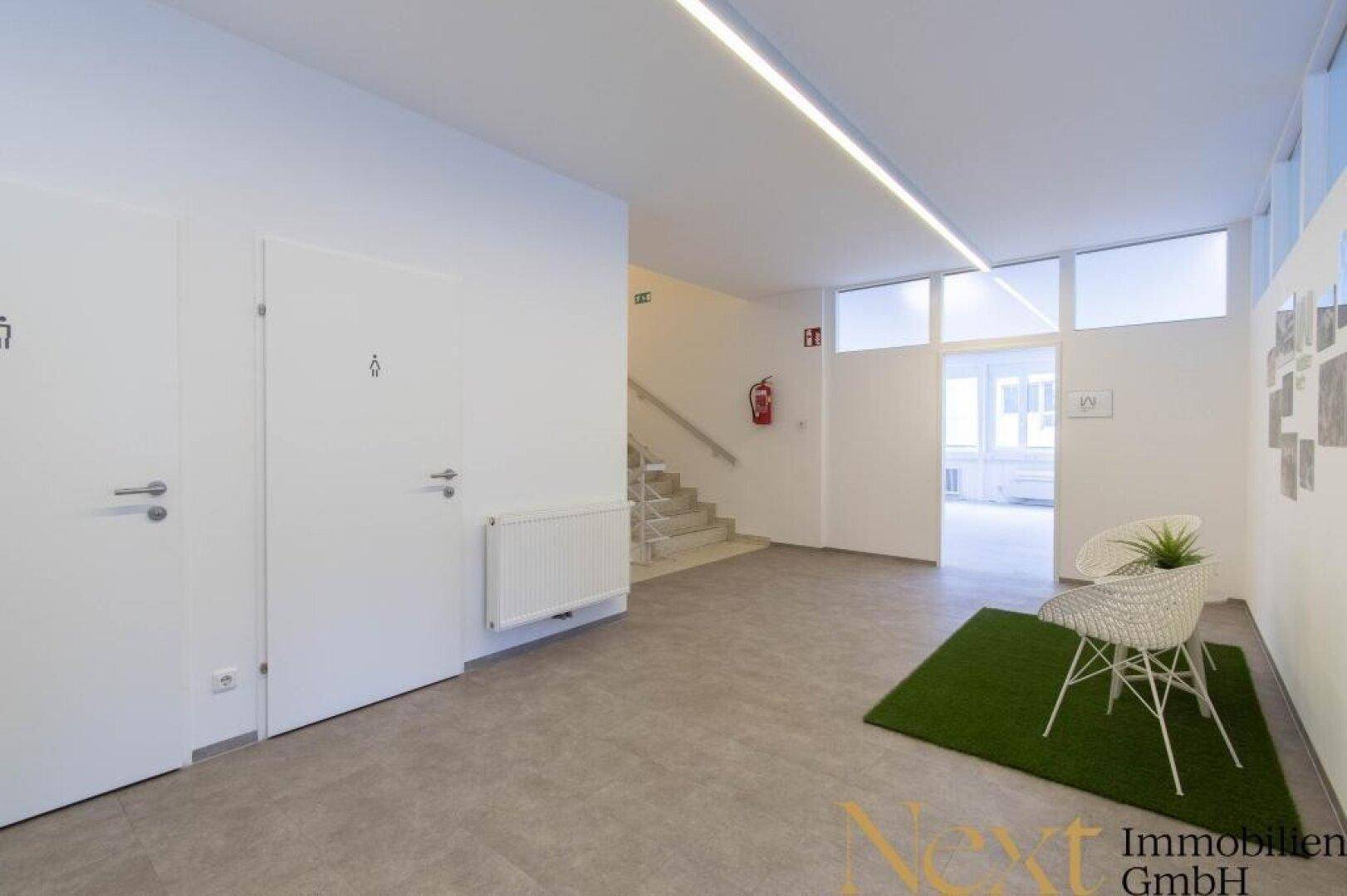 Moderner Flurbereich mit hellen Wänden, linearen Deckenleuchten und Zugang zu den Toiletten und Treppenhaus.