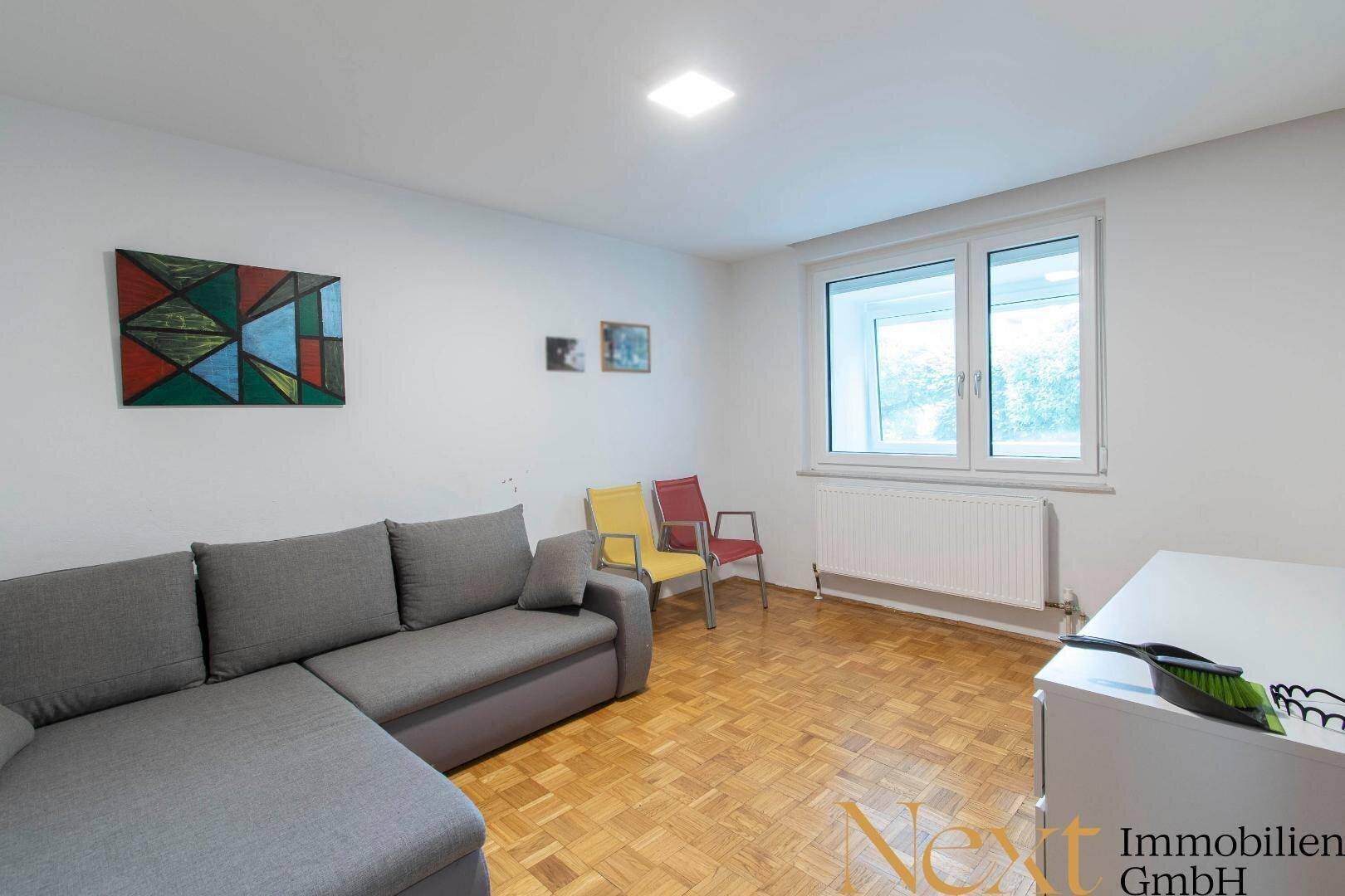 Gemütliches Wohnzimmer mit grauem Ecksofa, Holzboden und großem Fenster.