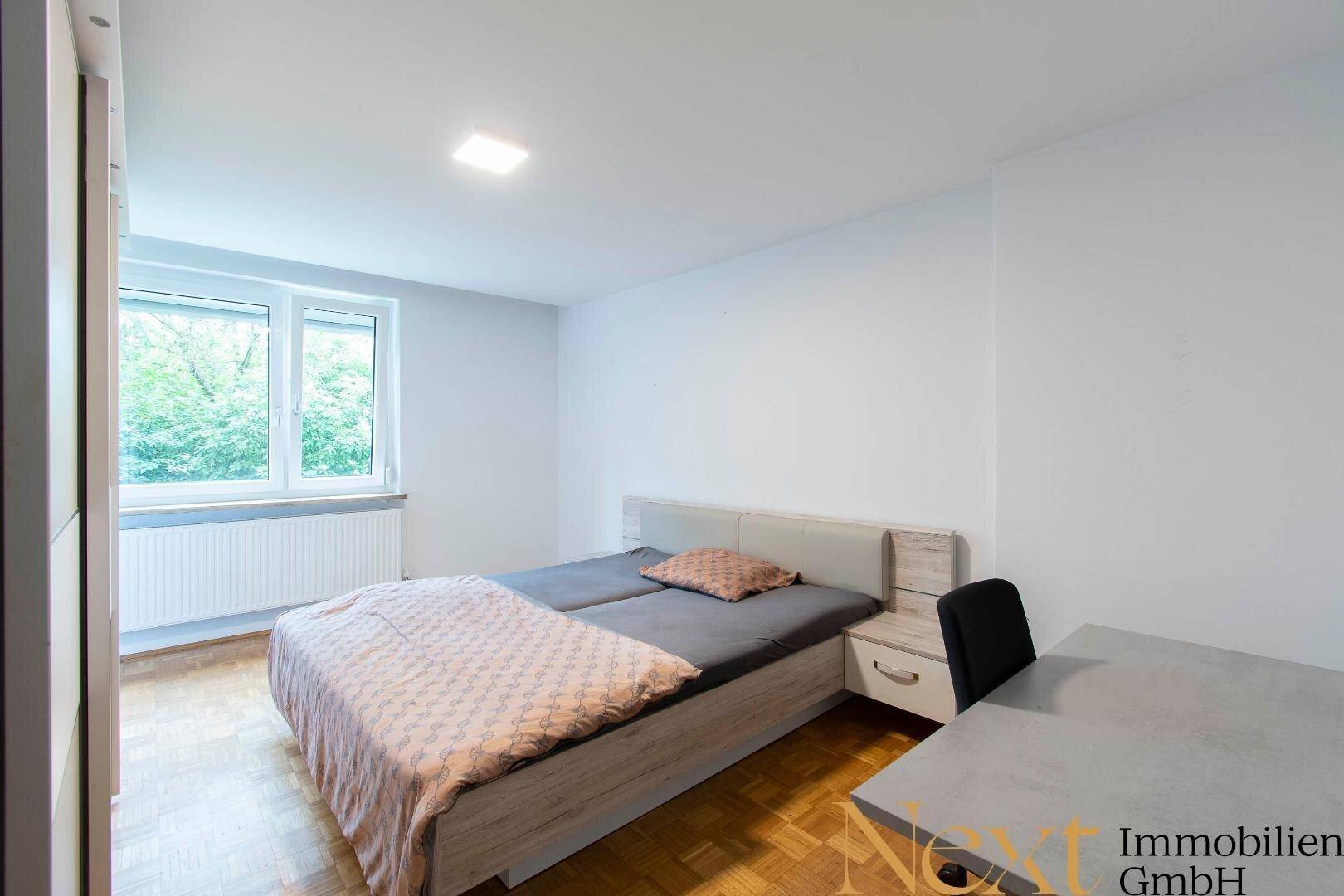 Schlafzimmer mit Doppelbett, Holzboden und großem Fenster mit Blick ins Grüne.