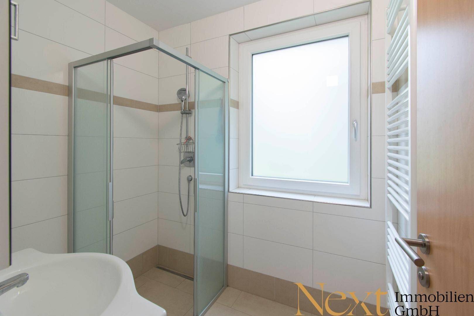 Helles Badezimmer mit Duschkabine, Waschbecken und beheiztem Handtuchhalter.