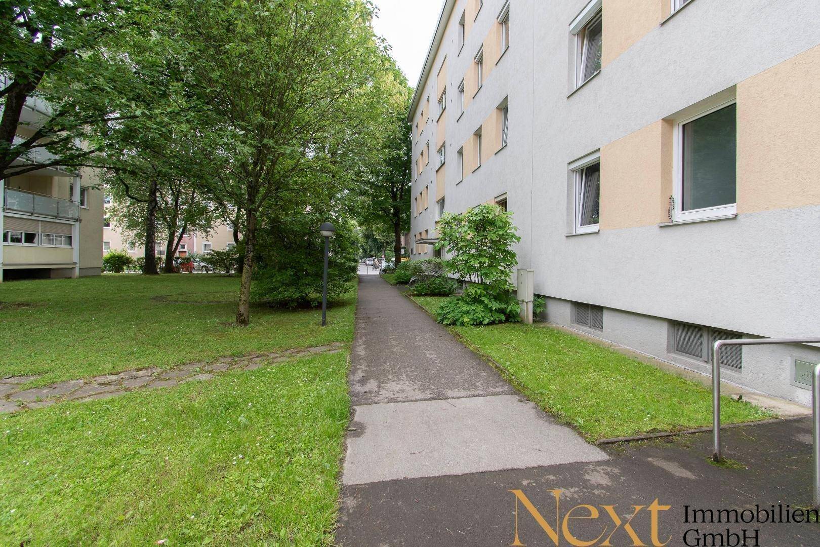 Gepflegte Außenanlage mit Gehwegen, Rasen und Bäumen entlang des Gebäudes.