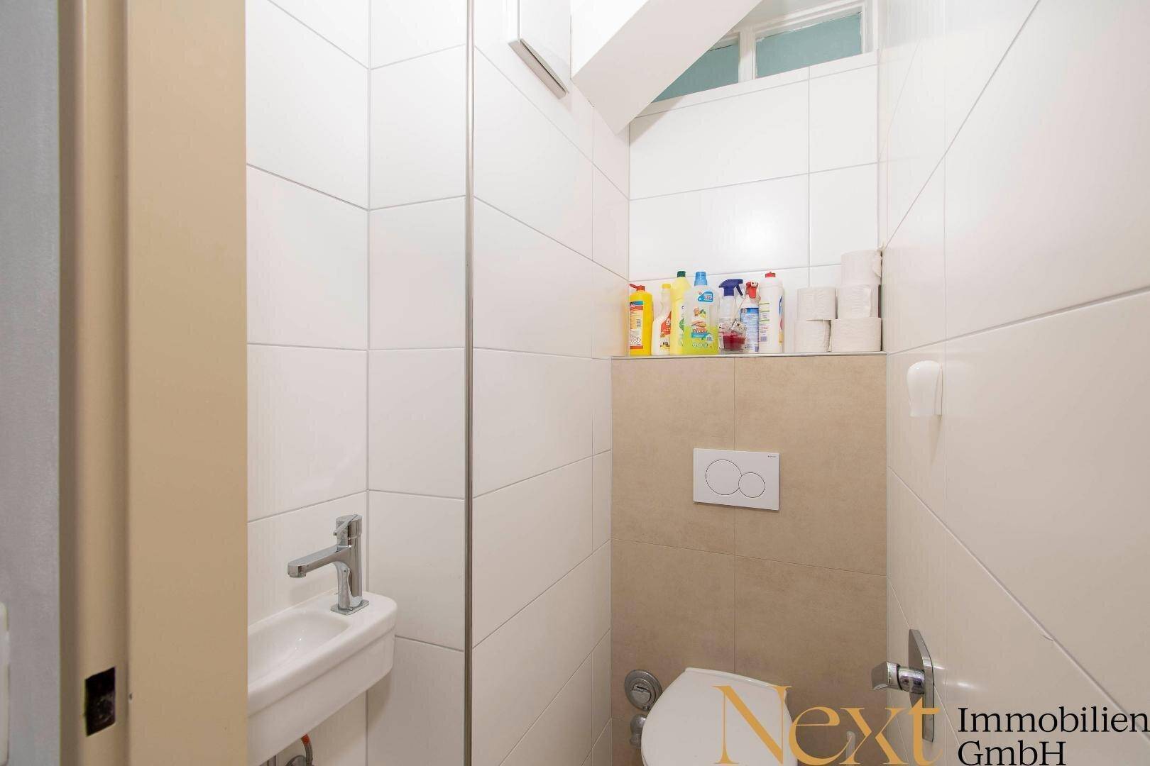 Separates WC mit wandhängender Toilette und kleinem Handwaschbecken.