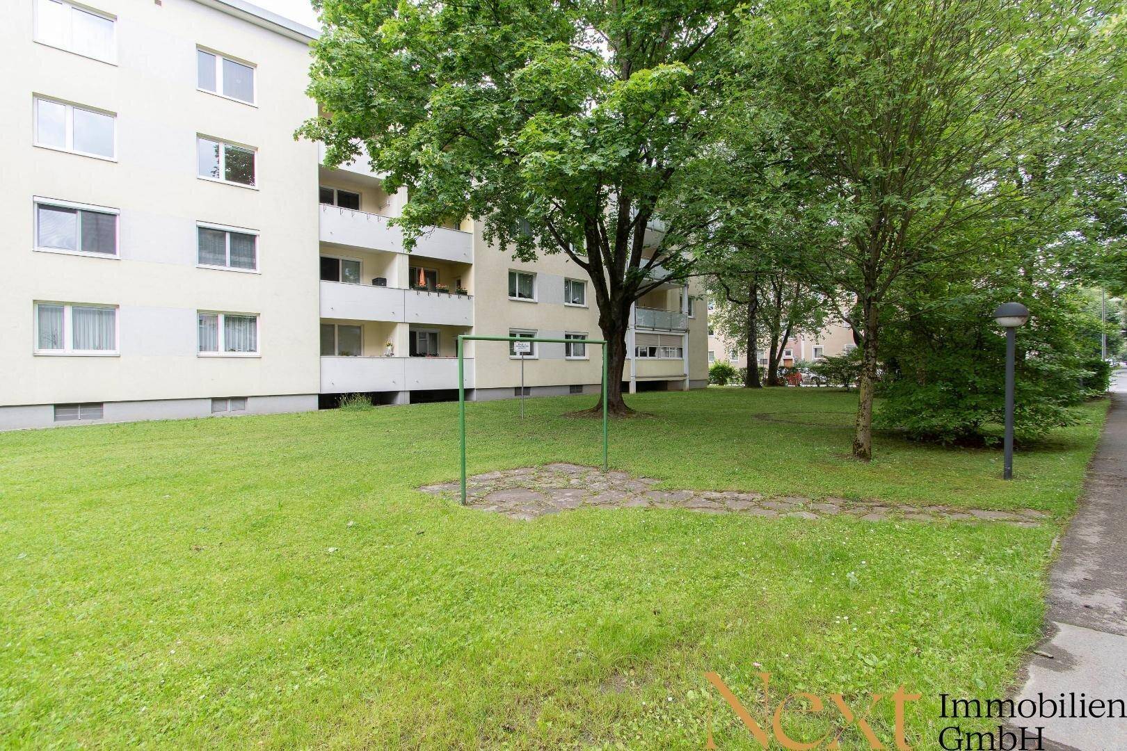 Grüne Außenanlage mit Rasenfläche und Bäumen vor einem Mehrfamilienhaus.