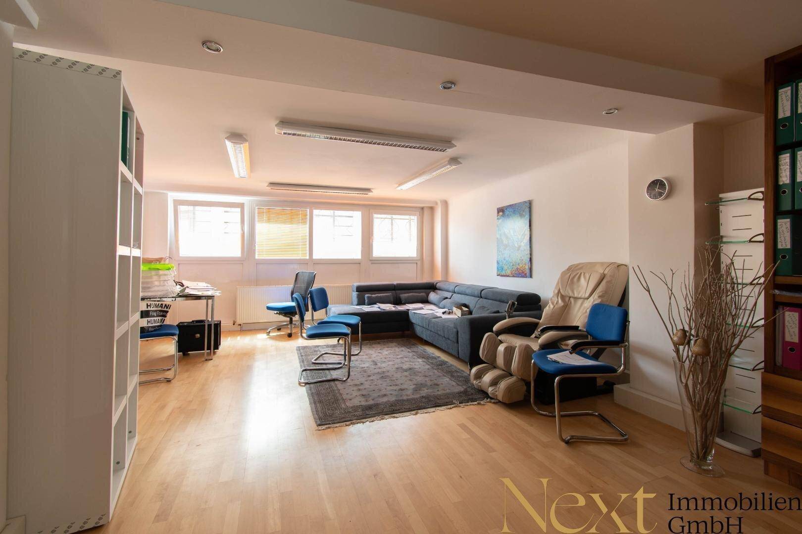 Heller Büroraum mit Holzboden, großer Couch und Massagesessel, bietet eine entspannte Arbeitsatmosphäre.