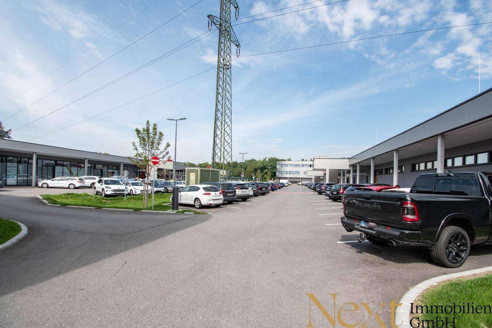 Großer Parkplatz eines Einkaufszentrums mit vielen Fahrzeugen und moderner Architektur im Hintergrund.