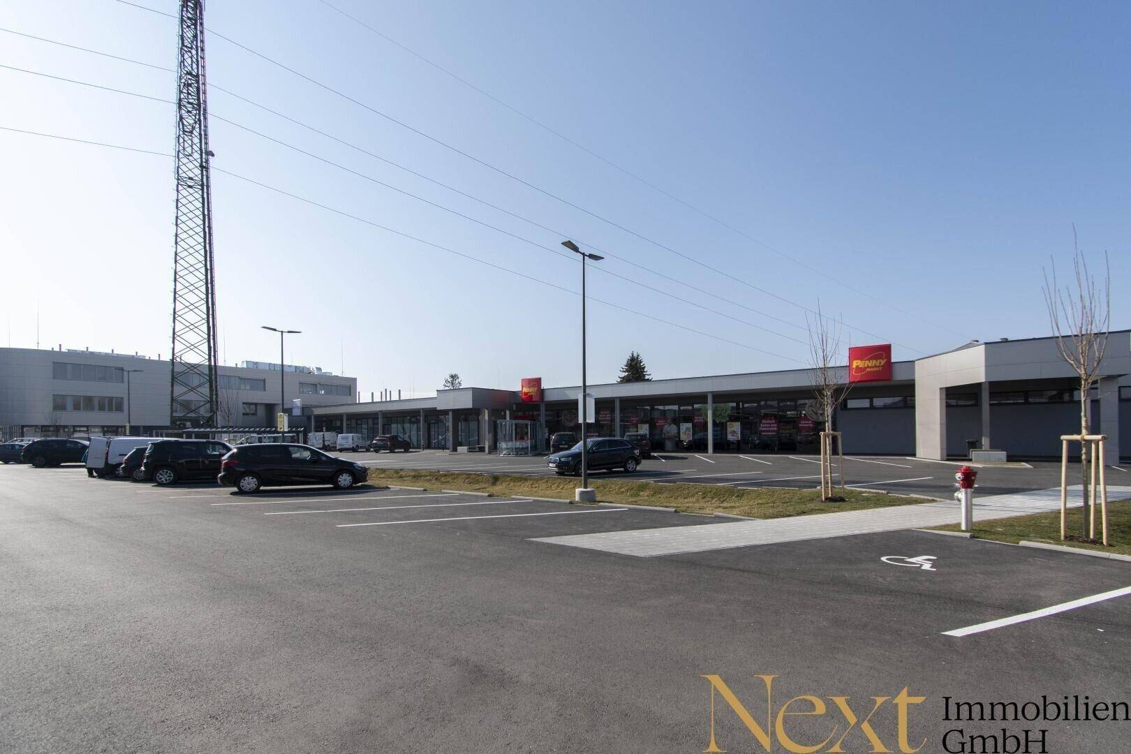 Weitläufiger Parkplatzbereich vor einem modernen Einkaufszentrum mit verschiedenen Geschäften.