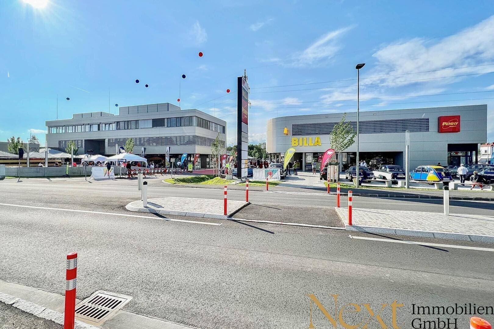 Weitläufige Ansicht eines modernen Einkaufszentrums mit Supermärkten und Bürogebäuden unter blauem Himmel.