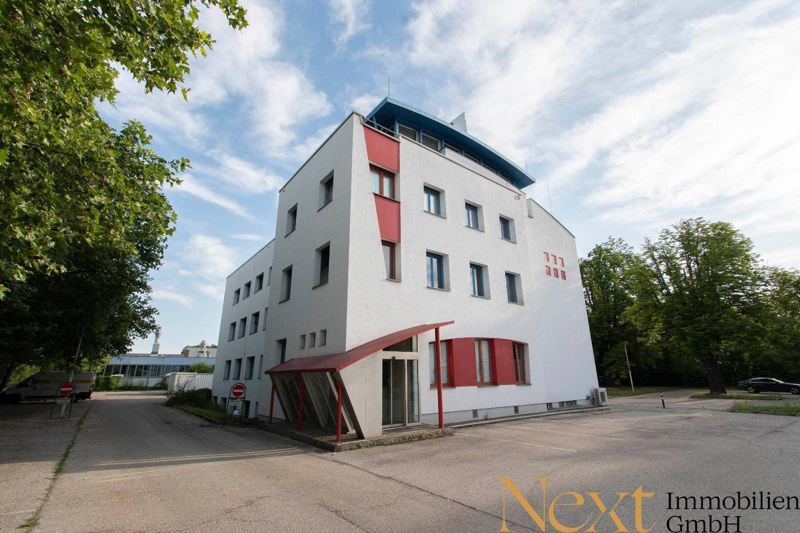 Modernes Bürogebäude mit weißer Fassade und roten Akzenten unter blauem Himmel.