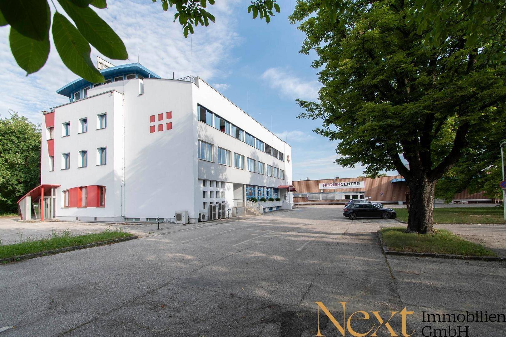 Gesamtansicht des modernen Bürokomplexes mit Parkplätzen und umliegender Grünfläche.