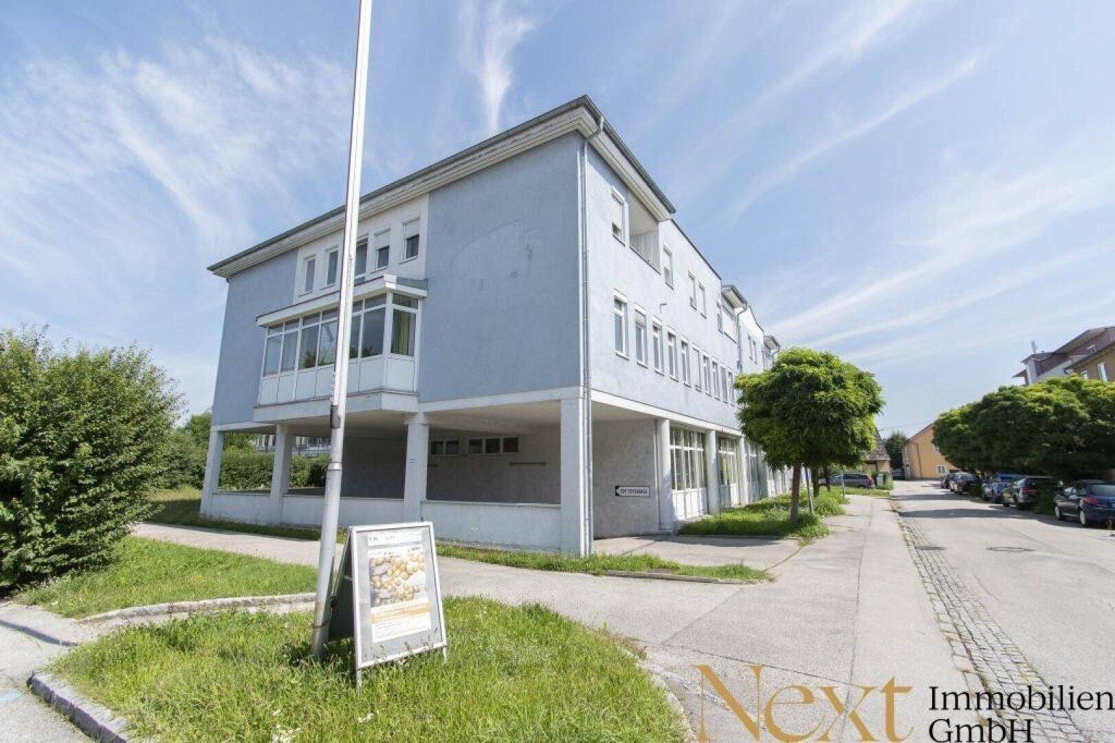 Ansicht eines modernen Bürogebäudes mit mehreren Etagen und umliegender Grünfläche.
