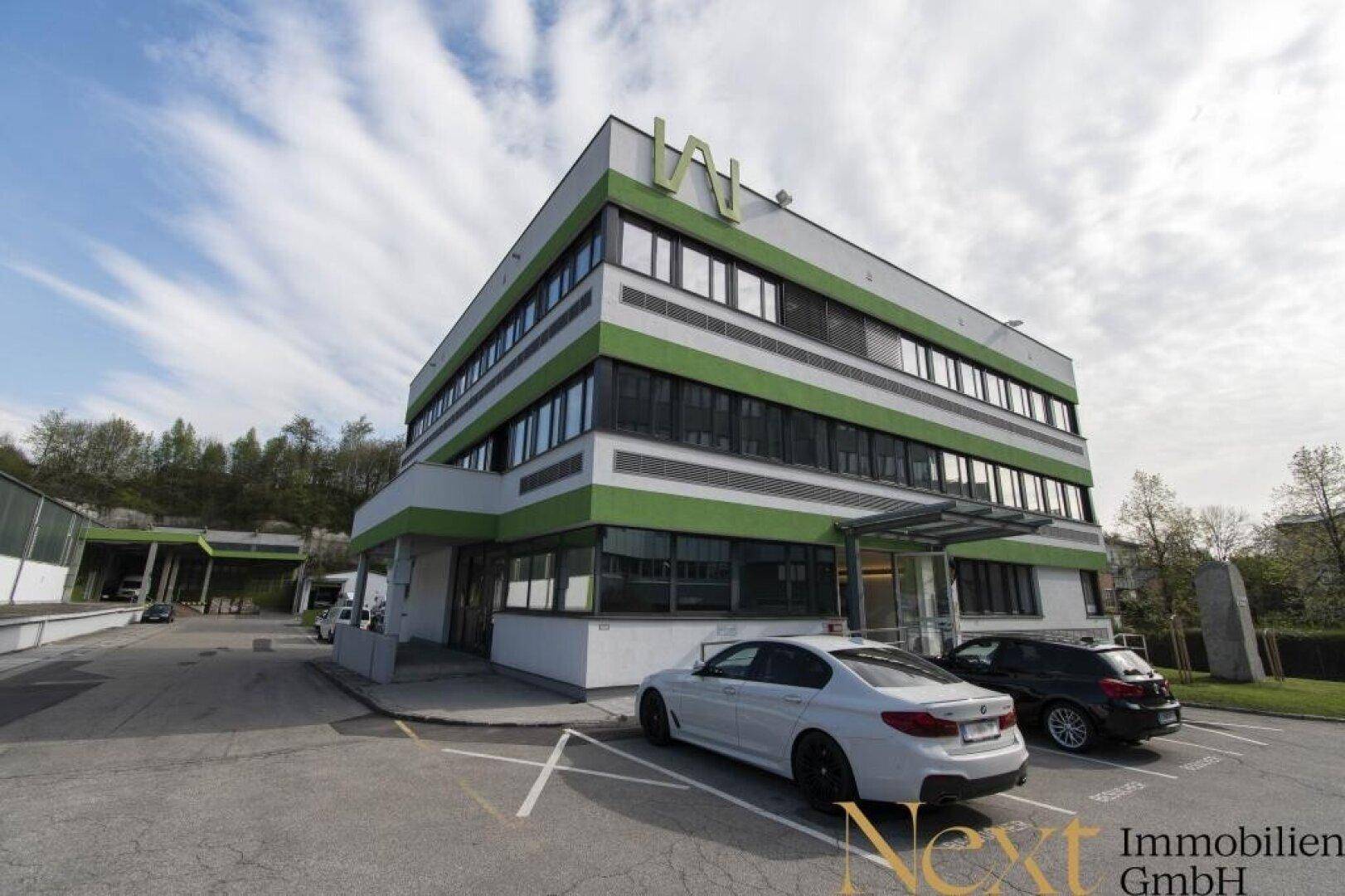 Modernes Bürogebäude mit grünen Akzenten an der Fassade und ausreichend Parkmöglichkeiten für Mitarbeiter und Besucher.