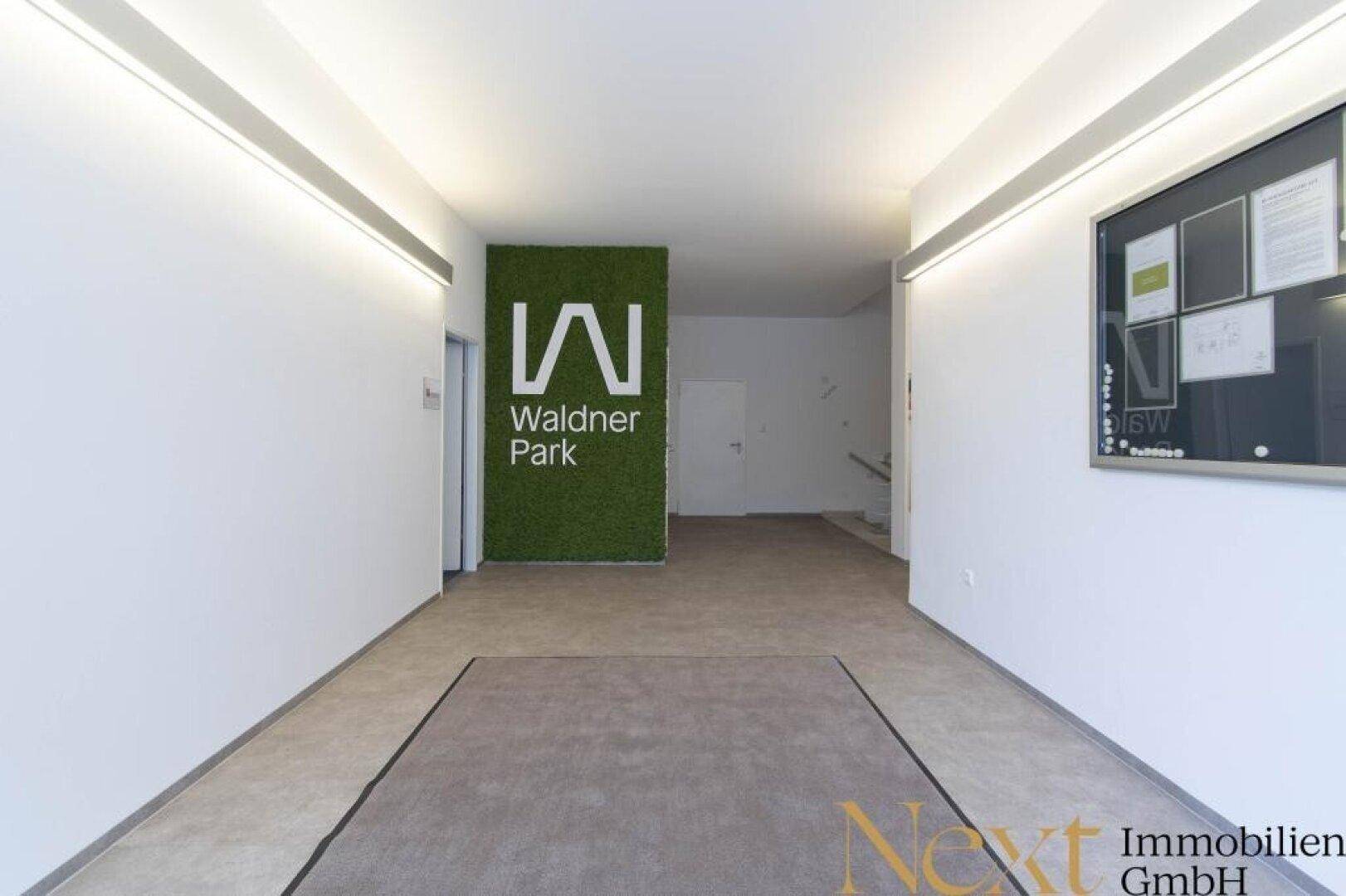 Moderner Empfangsbereich mit Firmenlogo auf einer begrünten Wand und Zugang zu weiteren Räumlichkeiten.