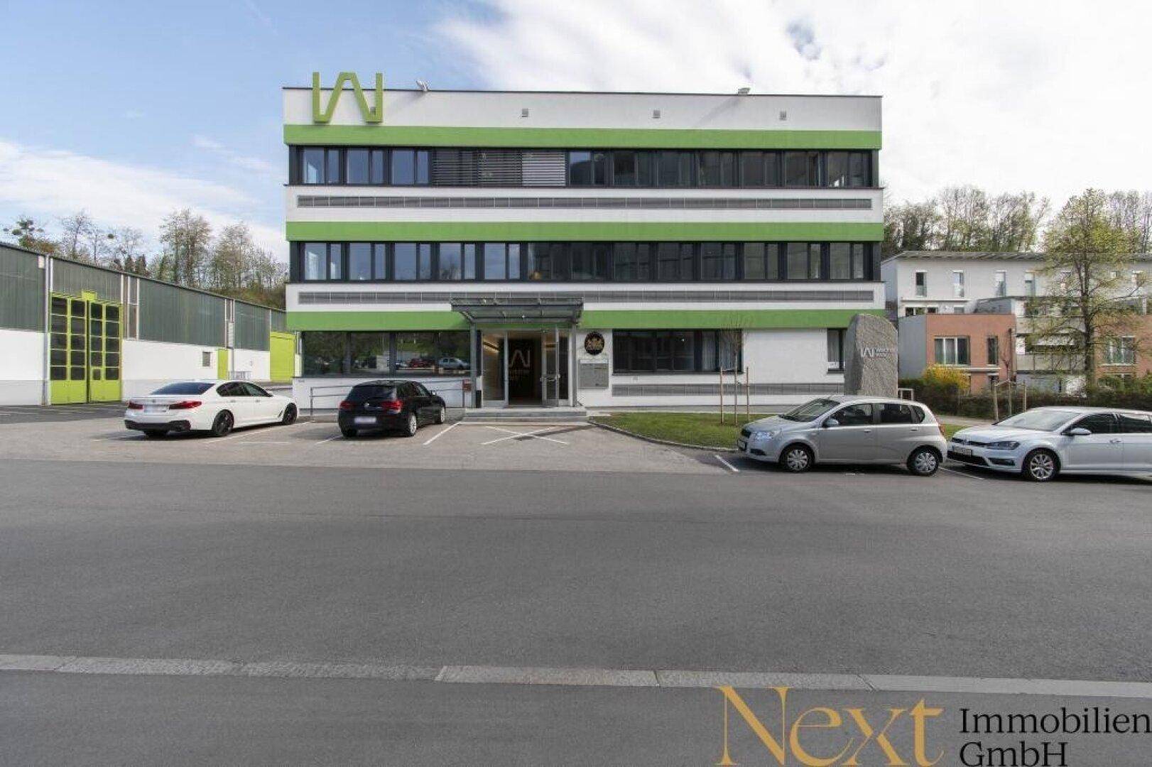 Ansicht des modernen Bürogebäudes mit markanter grüner Fassadengestaltung und großem Parkplatzbereich.