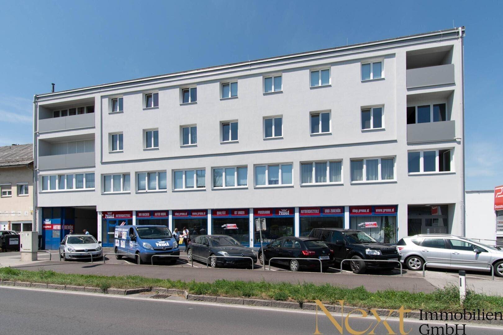 Modernes Geschäftsgebäude mit mehreren Etagen, großen Fenstern und Parkplätzen davor.