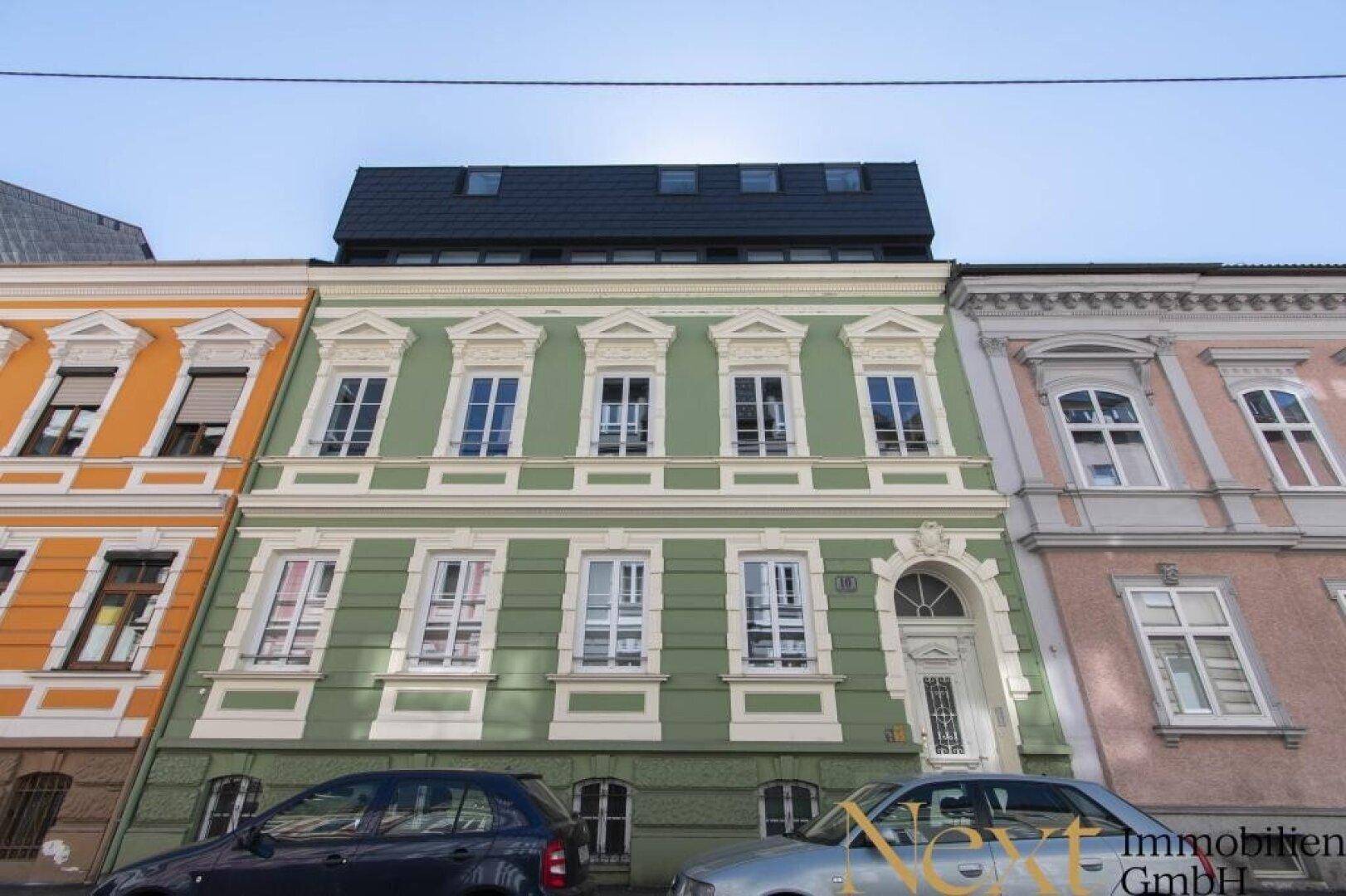 Historische Fassade eines Mehrfamilienhauses mit grüner Farbgebung und modernen Dachgauben.