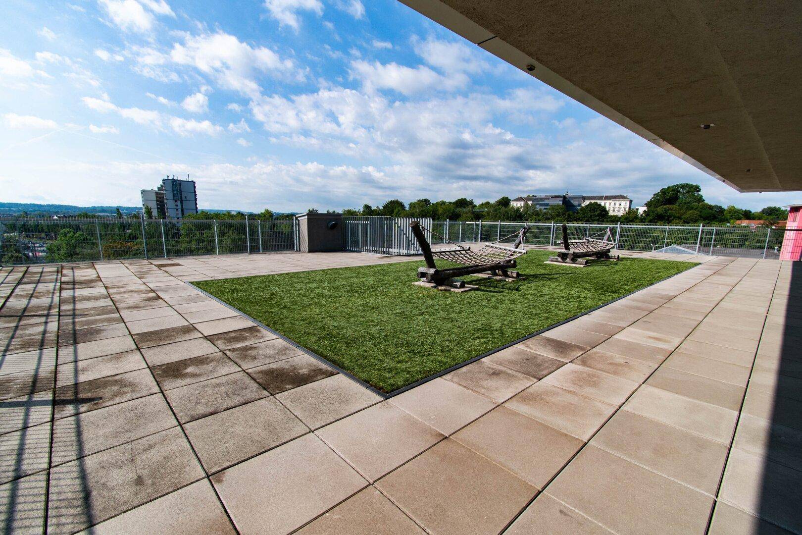 Weitläufige Dachterrasse mit Kunstrasen und Liegestühlen, bietet einen weiten Blick über die Umgebung.