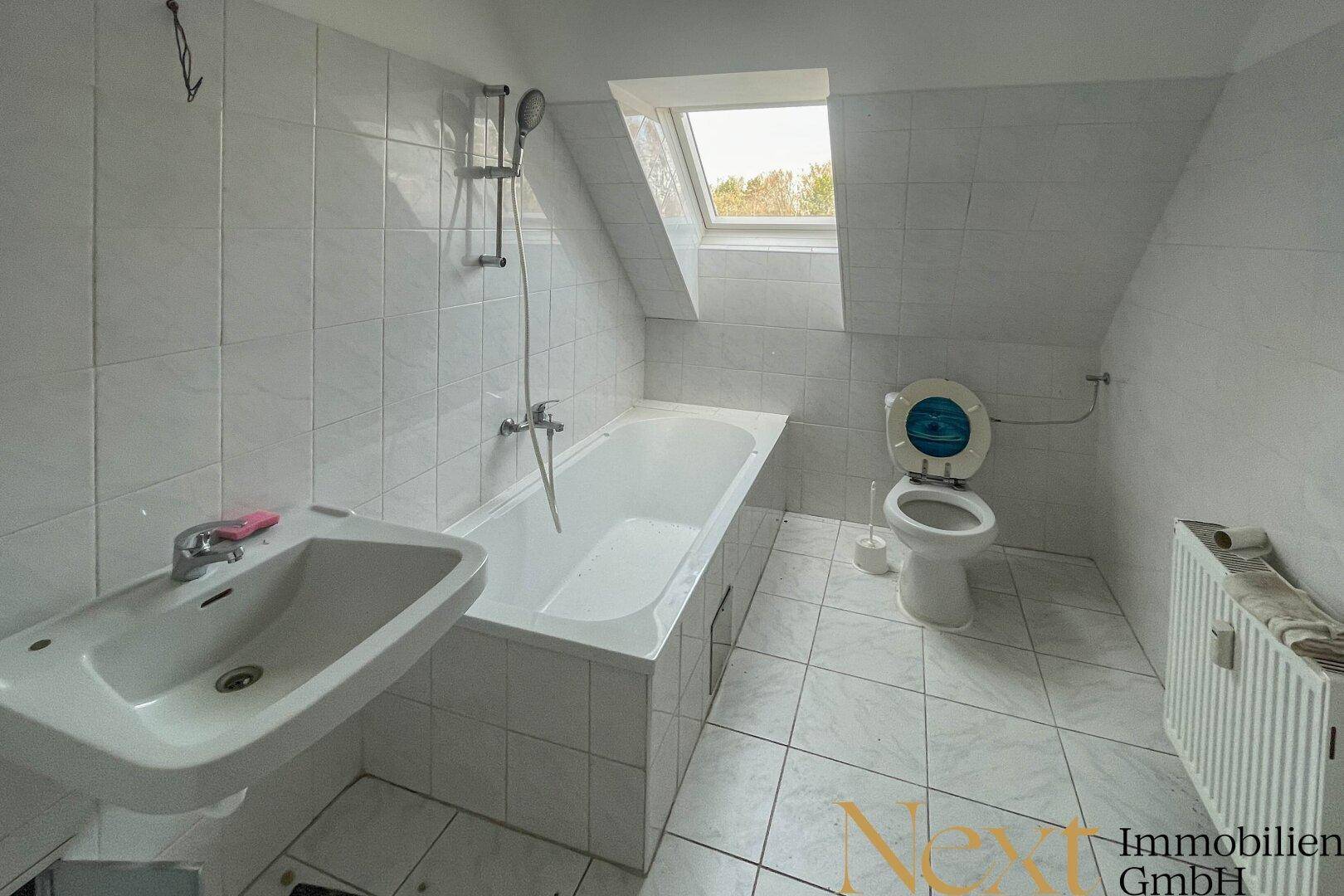 Gefliestes Badezimmer mit Badewanne, Waschbecken und WC unter einem Dachfenster.