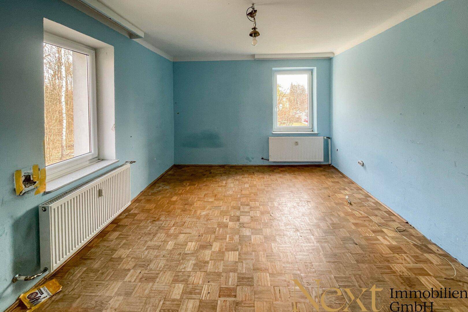 Helles Zimmer mit Parkettboden und blauen Wänden, bietet Potenzial für eine moderne Umgestaltung.