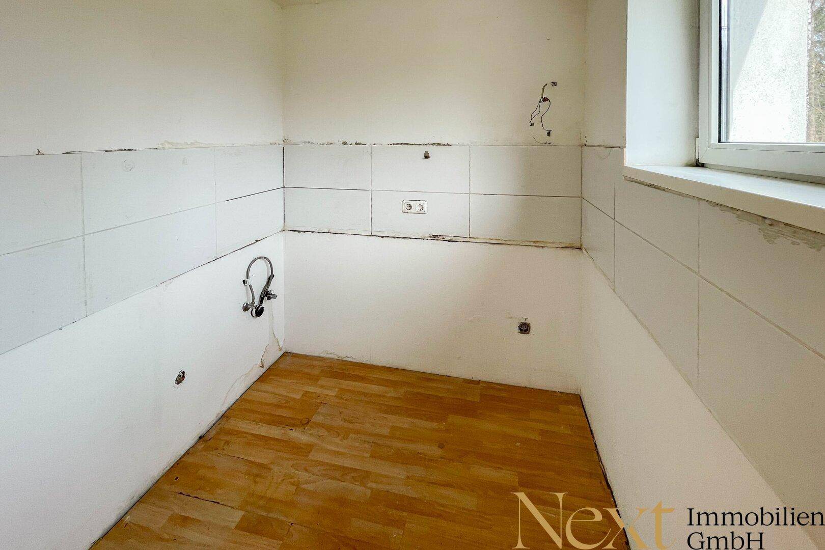 Leerer Küchenraum mit weißen Fliesen und Fenster, bereit für die Installation einer neuen Küche.