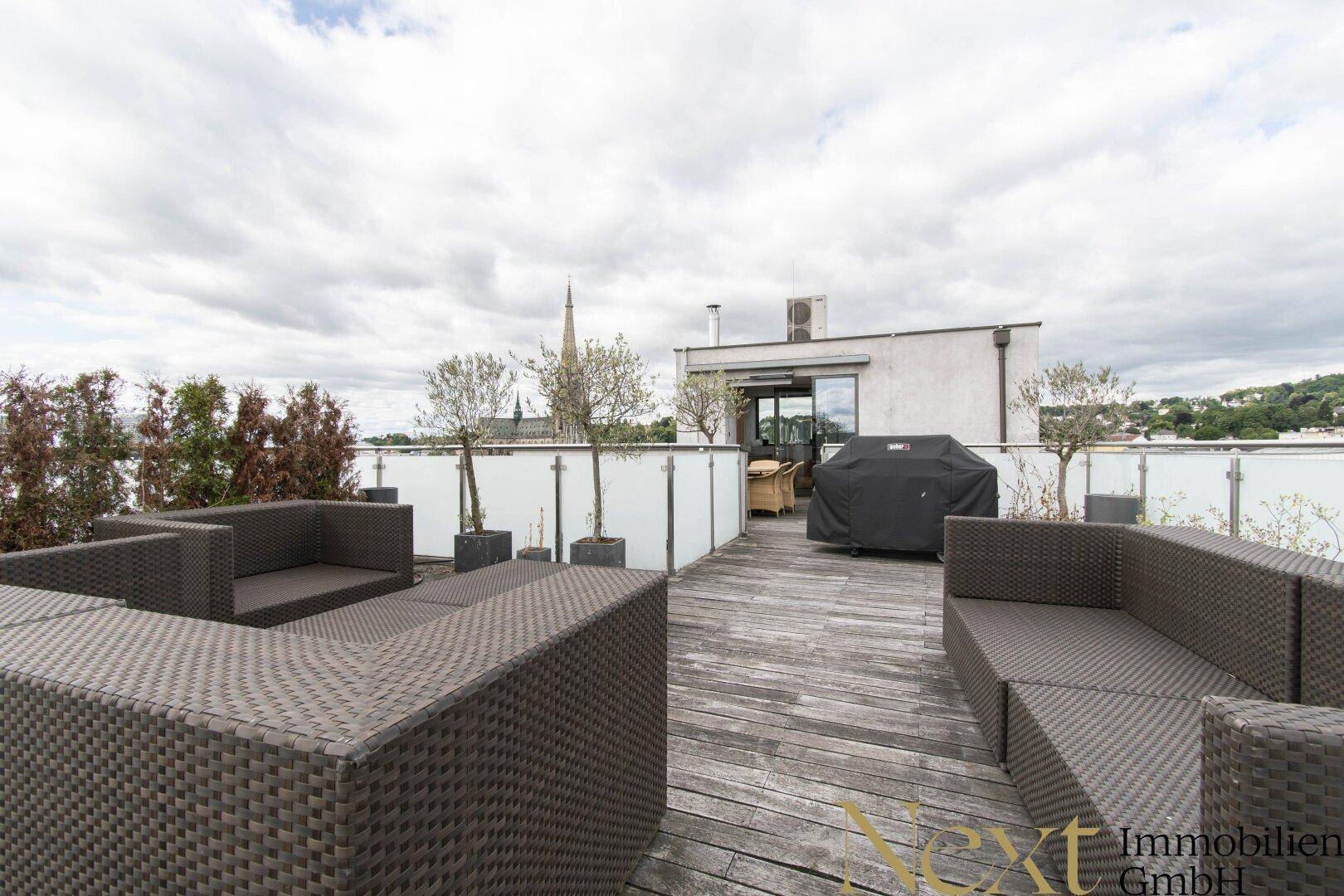 Geräumige Dachterrasse mit bequemen Loungemöbeln, Grill und Blick auf die Stadt.