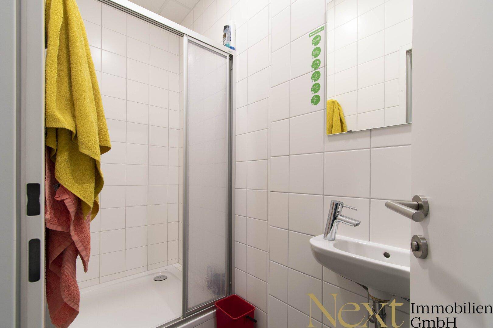 Kompaktes Badezimmer mit Duschkabine, Waschbecken und weißen Fliesen.
