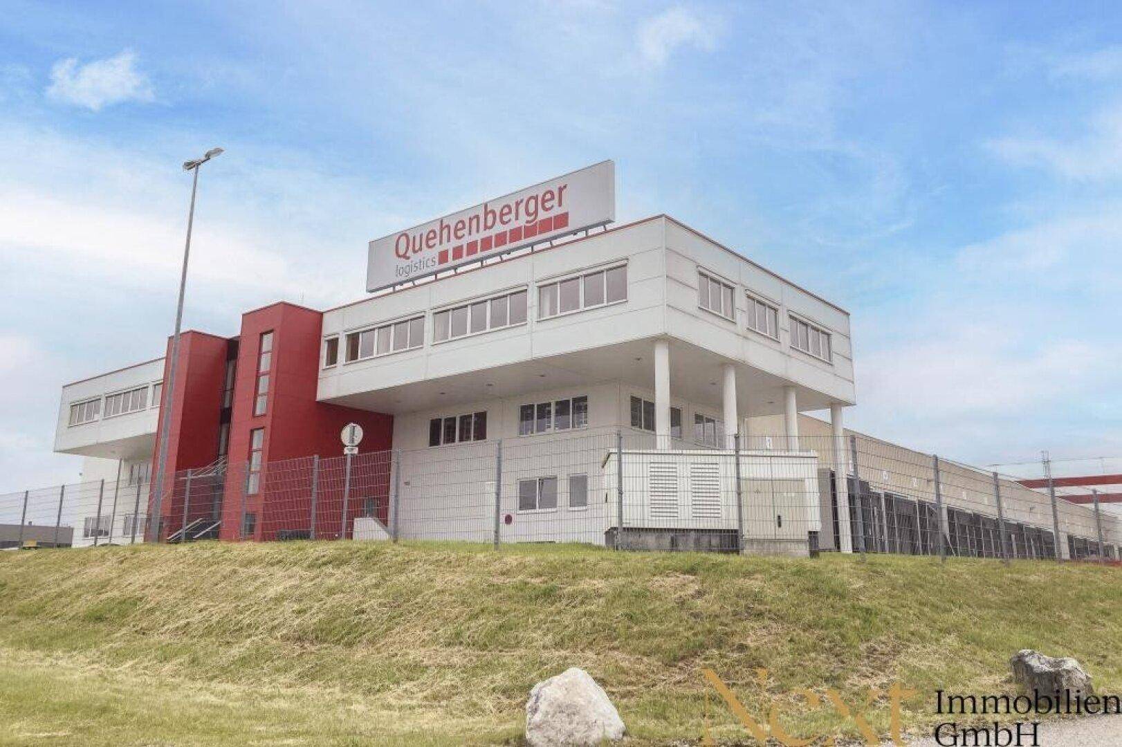 Modernes Logistikgebäude mit weißer Fassade, roten Akzenten und großen Fenstern unter blauem Himmel.