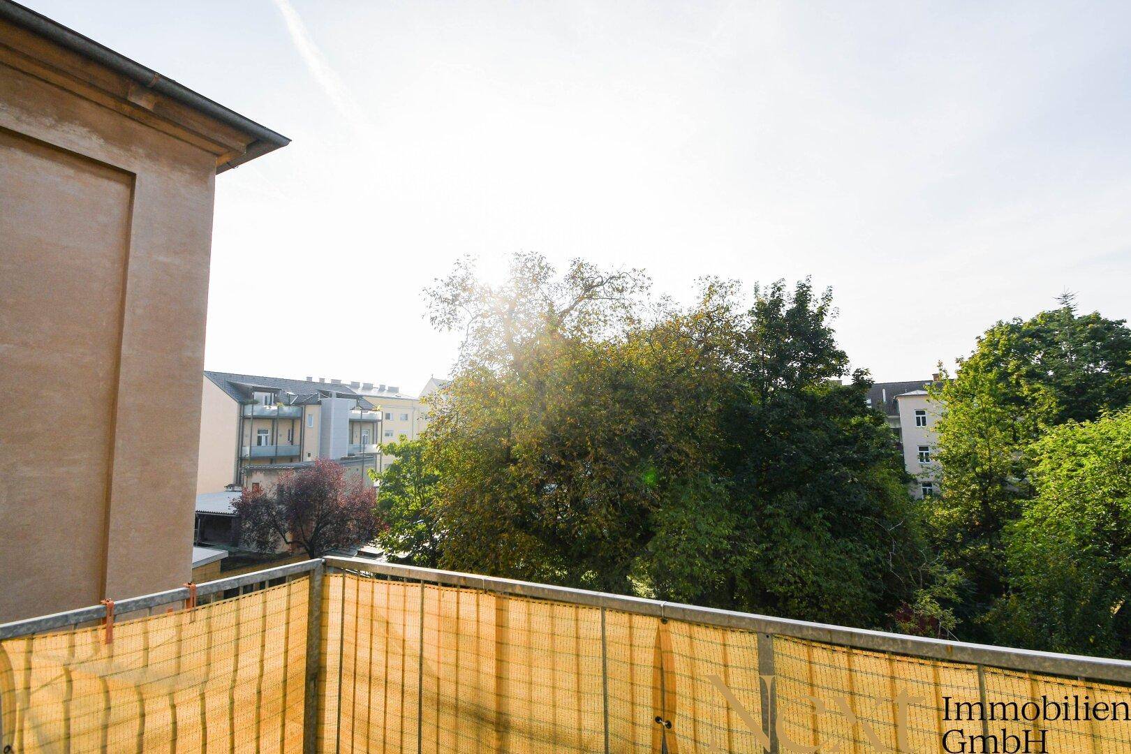 Sonniger Balkon mit Blick ins Grüne und auf umliegende Gebäude, ideal zum Entspannen.