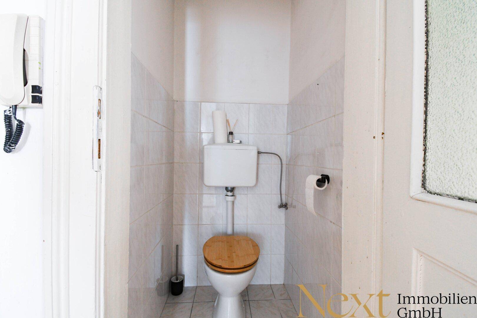 Separates WC mit Fliesen an den Wänden und einem Holz-Toilettensitz, funktional und hell.