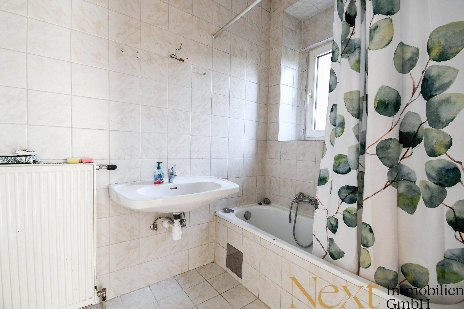 Gefliestes Badezimmer mit Badewanne, Waschbecken und Fenster, ausgestattet mit Duschvorhang.