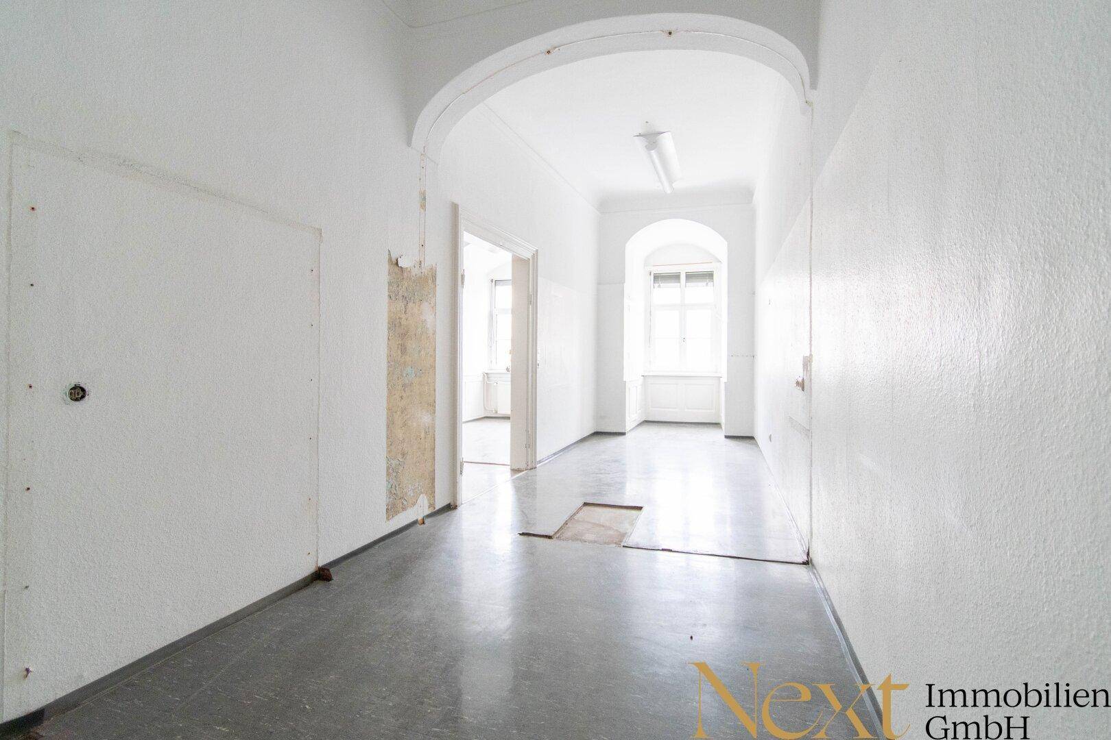 Langer Flur in einem Altbau mit hohen Decken und Renovierungsbedarf, der viel natürliches Licht erhält.