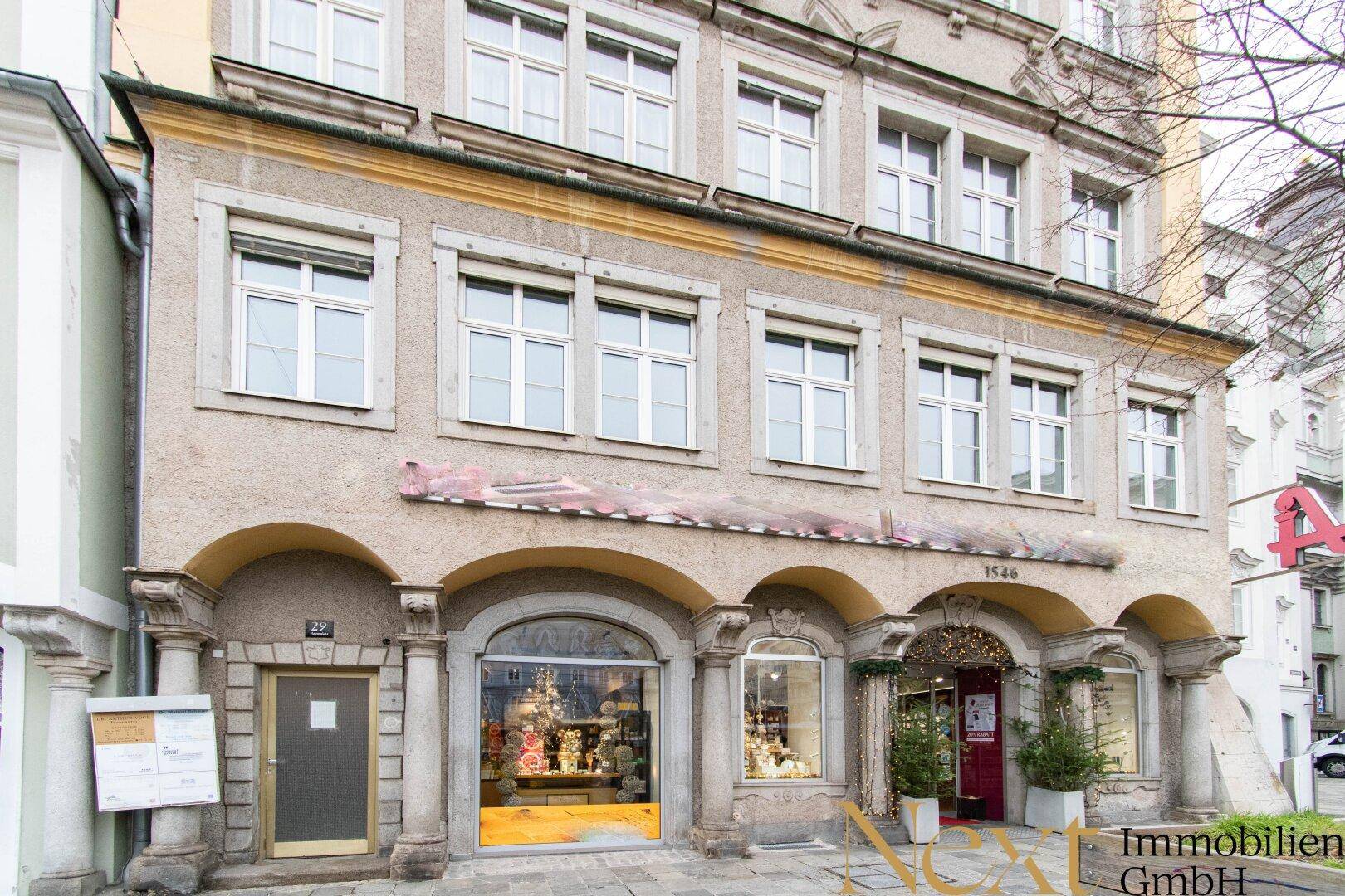 Historische Altbaufassade mit Arkaden und großen Schaufenstern im Erdgeschoss, die gut erhalten ist.