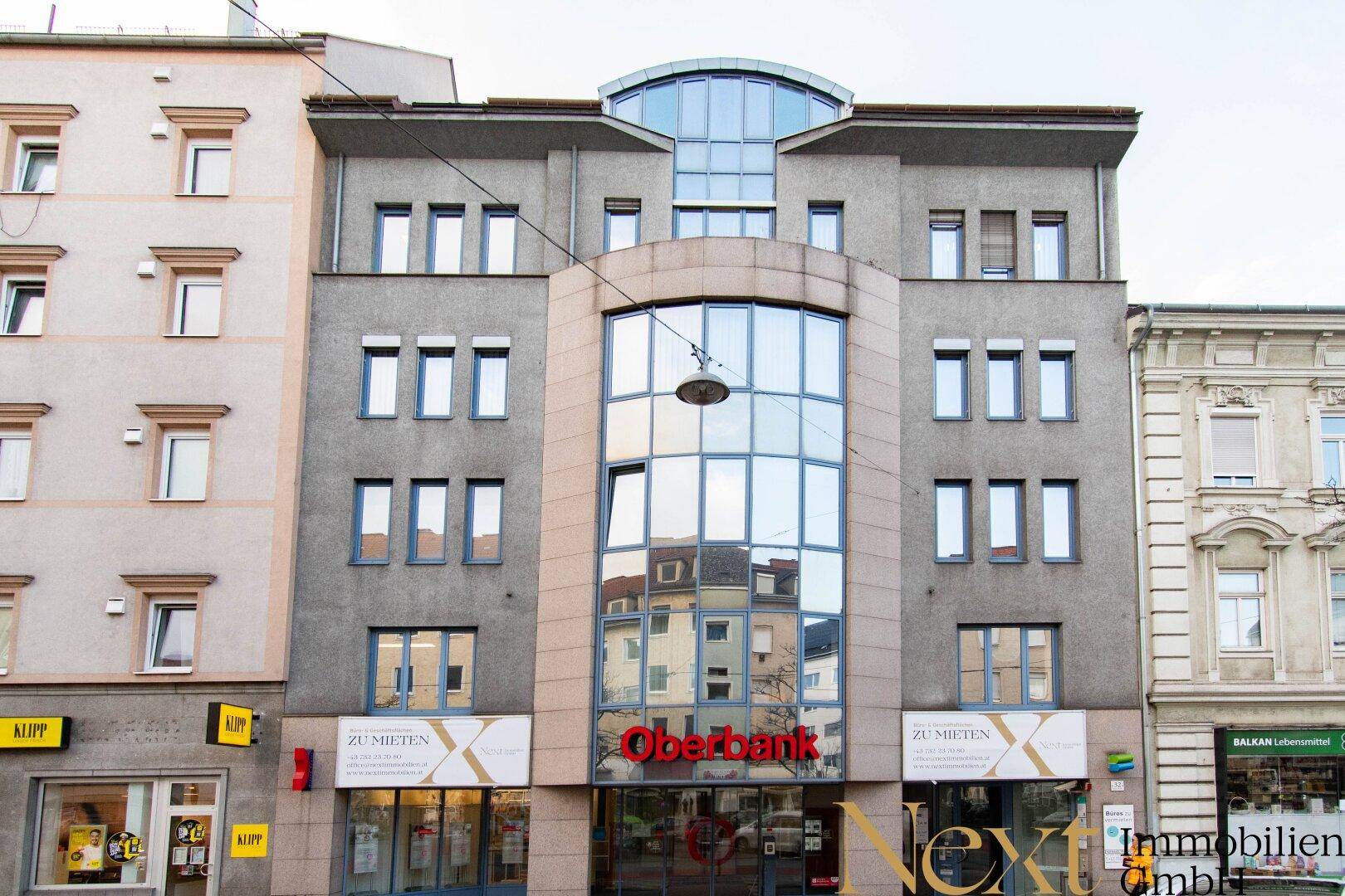 Modernes Geschäfts- und Wohngebäude mit markanter Glasfassade und großen Fenstern in städtischer Umgebung.