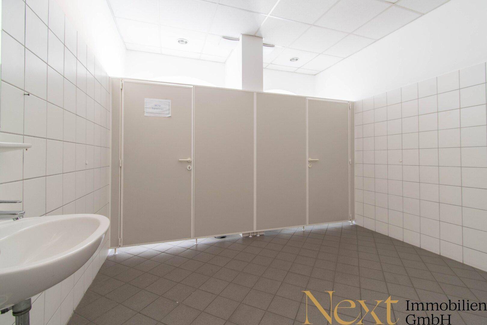 Sanitärbereich mit mehreren Toilettenkabinen, gefliesten Wänden und einem Waschbecken, in gutem Zustand.