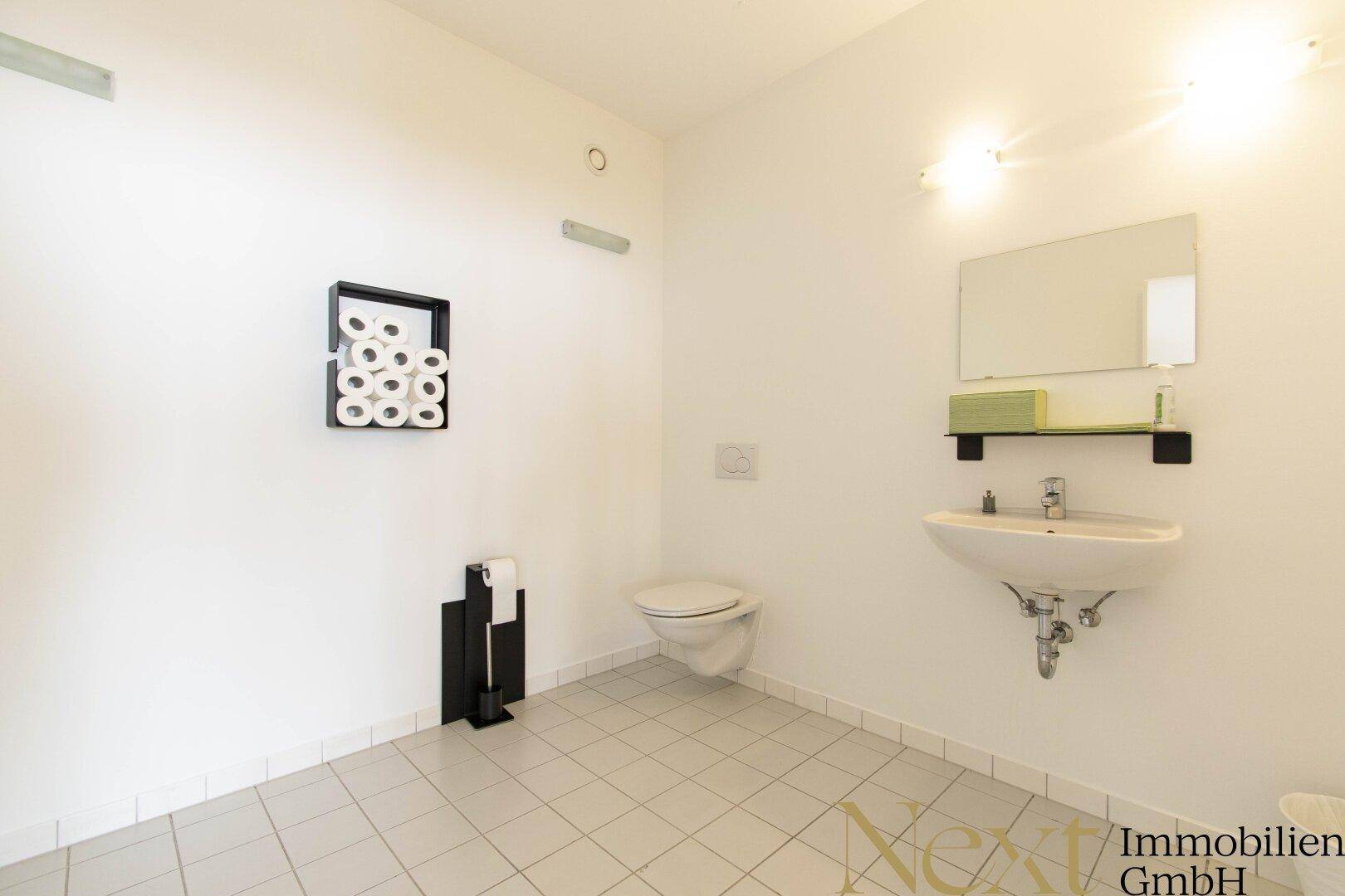 Saubere und helle Toilette mit Waschbecken, Spiegel und Fliesenboden in neutralen Farben.