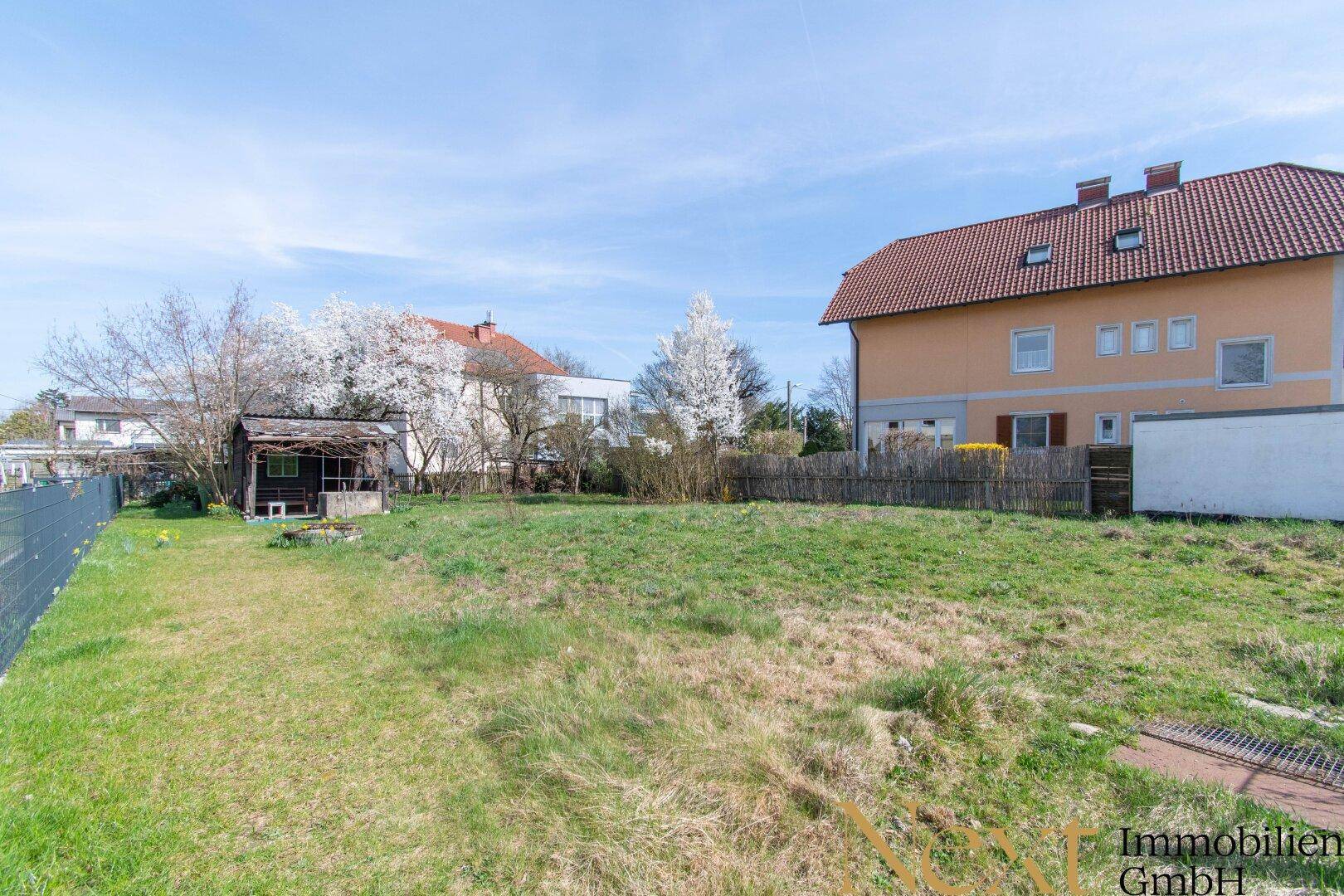 Weitläufiges Gartengrundstück mit Rasenfläche, kleinem Schuppen und blühenden Bäumen.