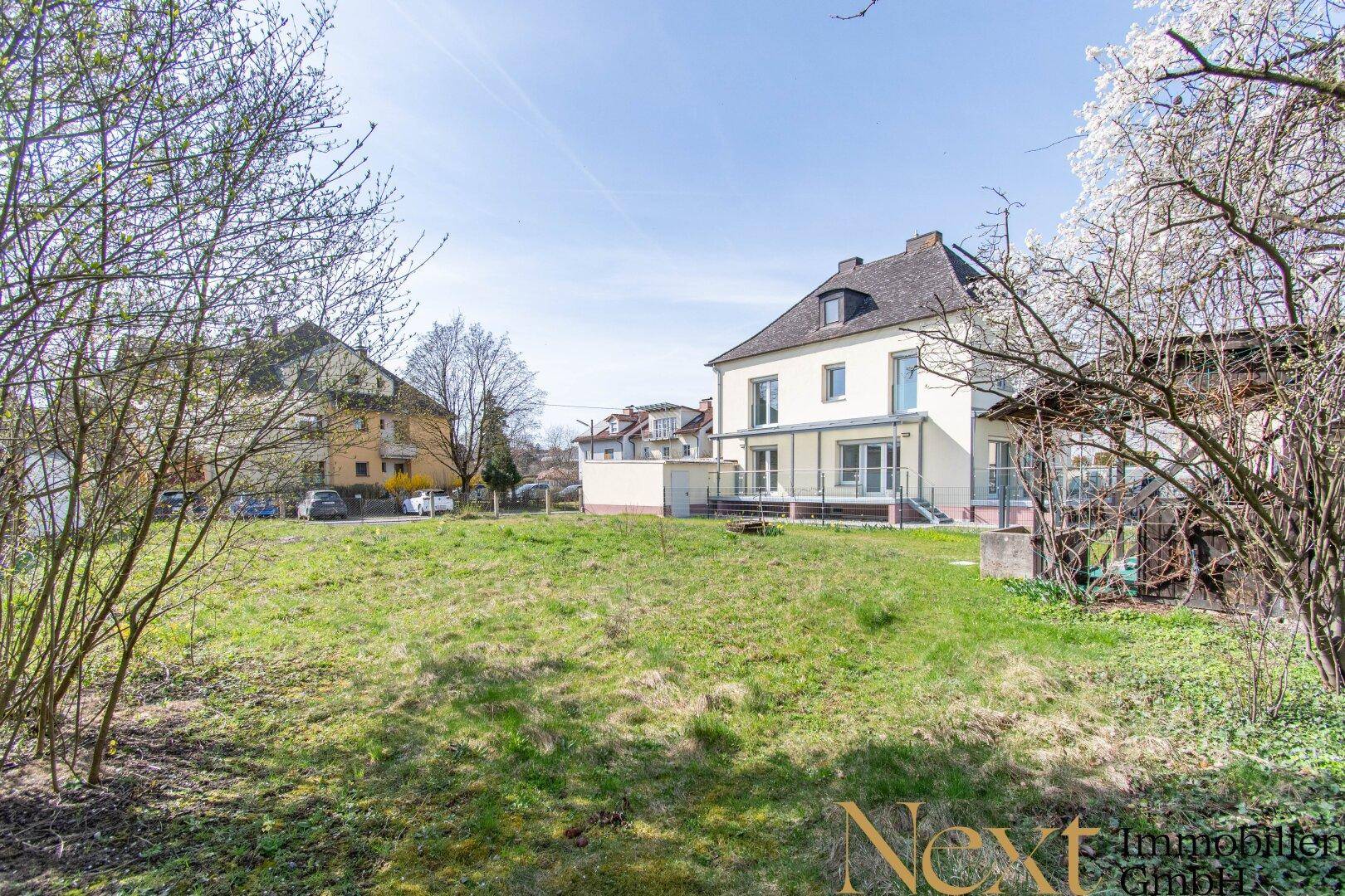 Gepflegtes Gartengrundstück mit Rasenfläche und Blick auf ein modernes Wohnhaus mit Terrasse.