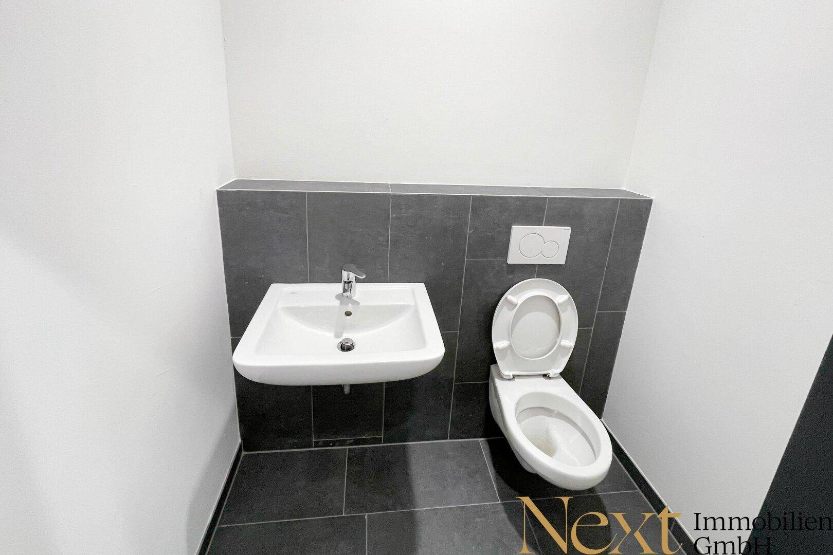 Saubere Gästetoilette mit Wand-WC und kleinem Waschbecken, modern gefliest.