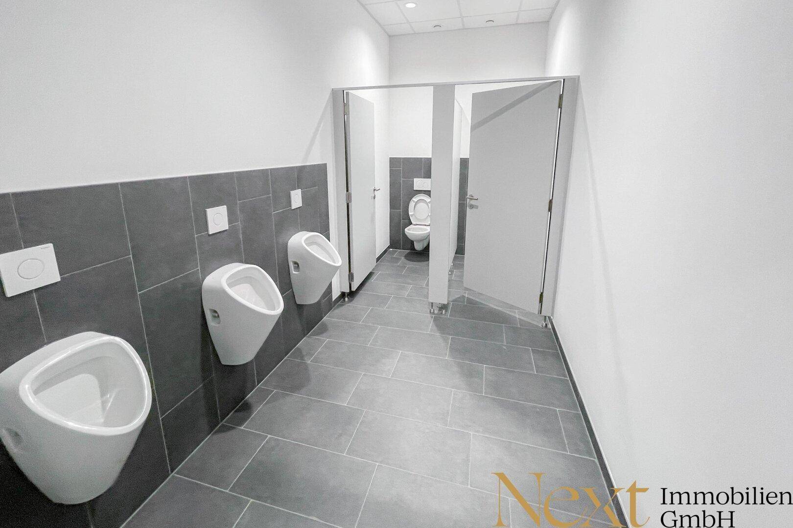 Geräumiger Herrenwaschraum mit mehreren Urinalen und separaten Toilettenkabinen.