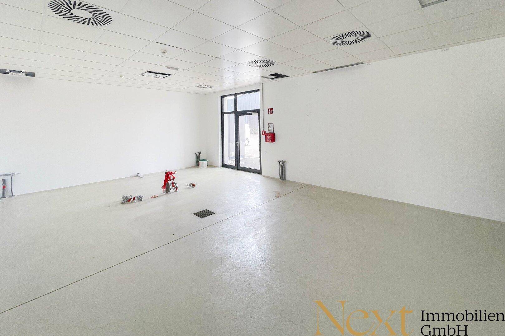 Großer, heller Raum mit abgehängter Decke, Lüftungsauslässen und Zugangstür.