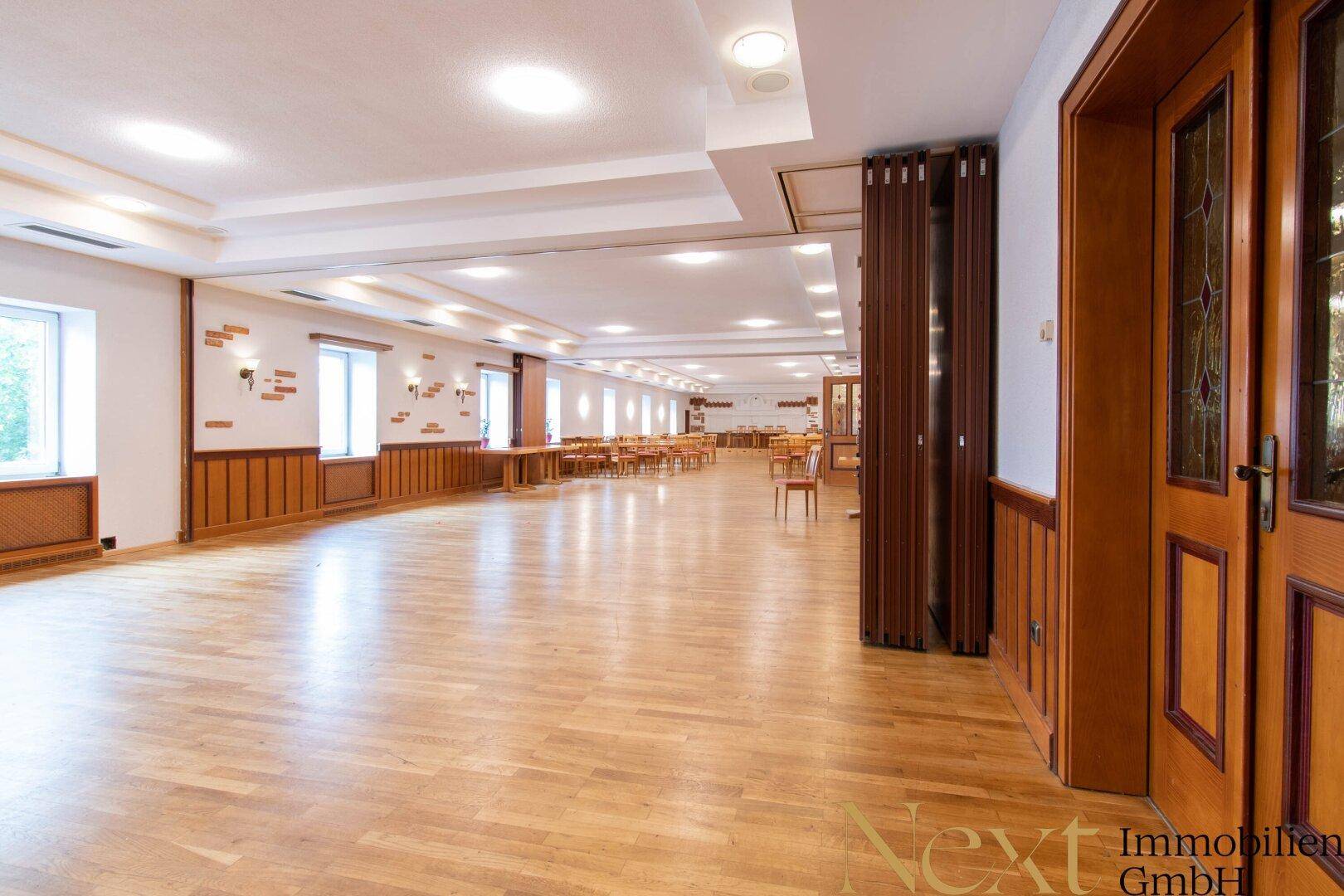 Großer, heller Saal mit Parkettboden, Holzvertäfelung und vielen Fenstern, ideal für Veranstaltungen.