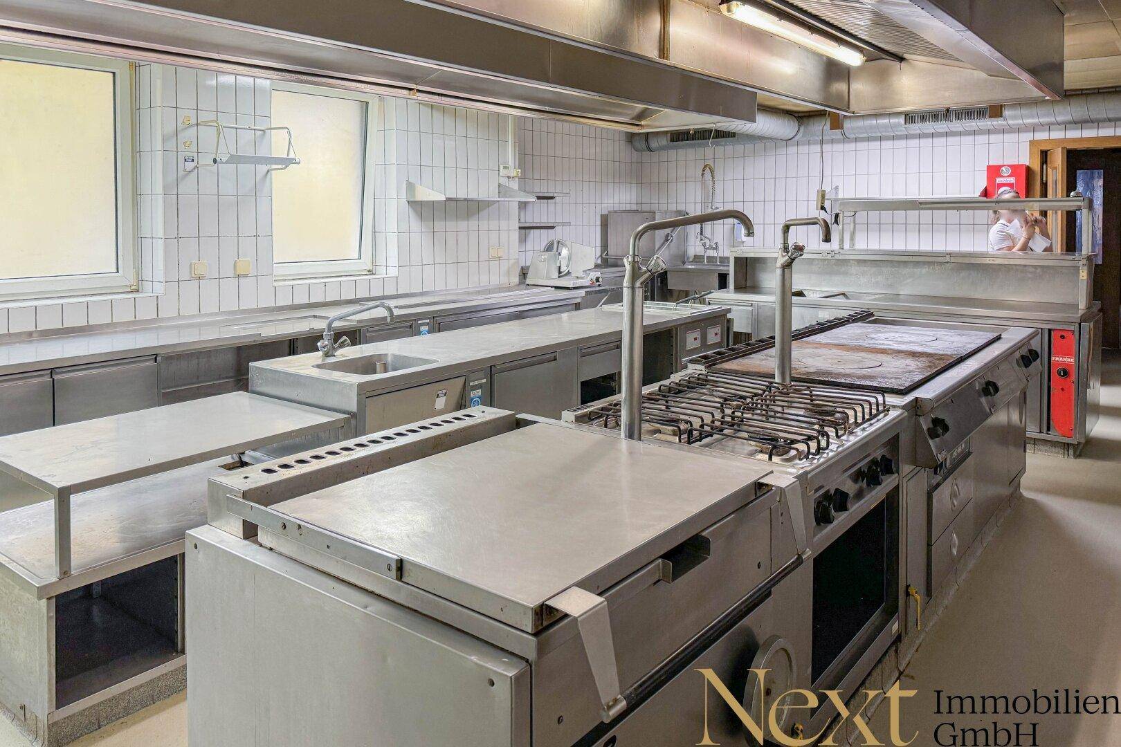 Große, professionelle Edelstahlküche mit mehreren Kochstationen und Fliesenwänden für den Gastronomiebetrieb.
