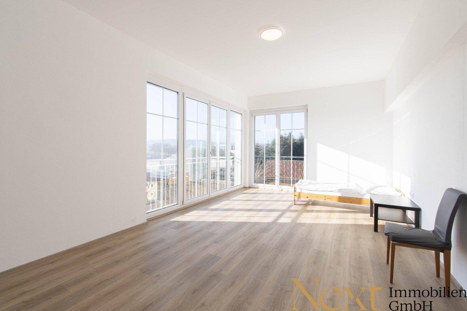 Helles Schlafzimmer mit Laminatboden, großen Fenstern und Zugang zu einem französischen Balkon.