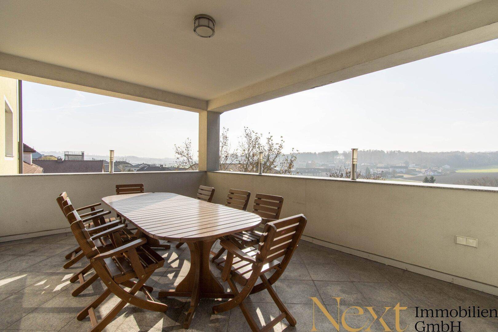 Geräumige überdachte Terrasse mit Holztisch und Stühlen, bietet einen weiten Blick in die Landschaft.